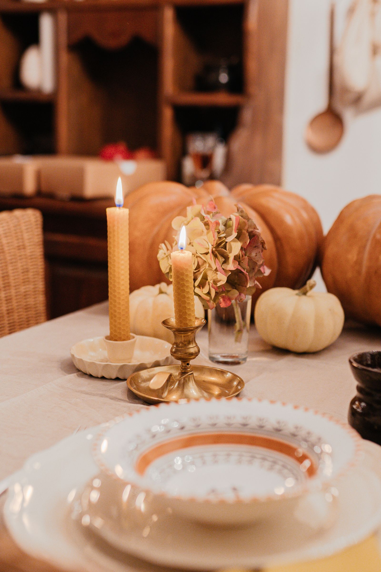 A dining table set with pumpkins, candles, and dishes