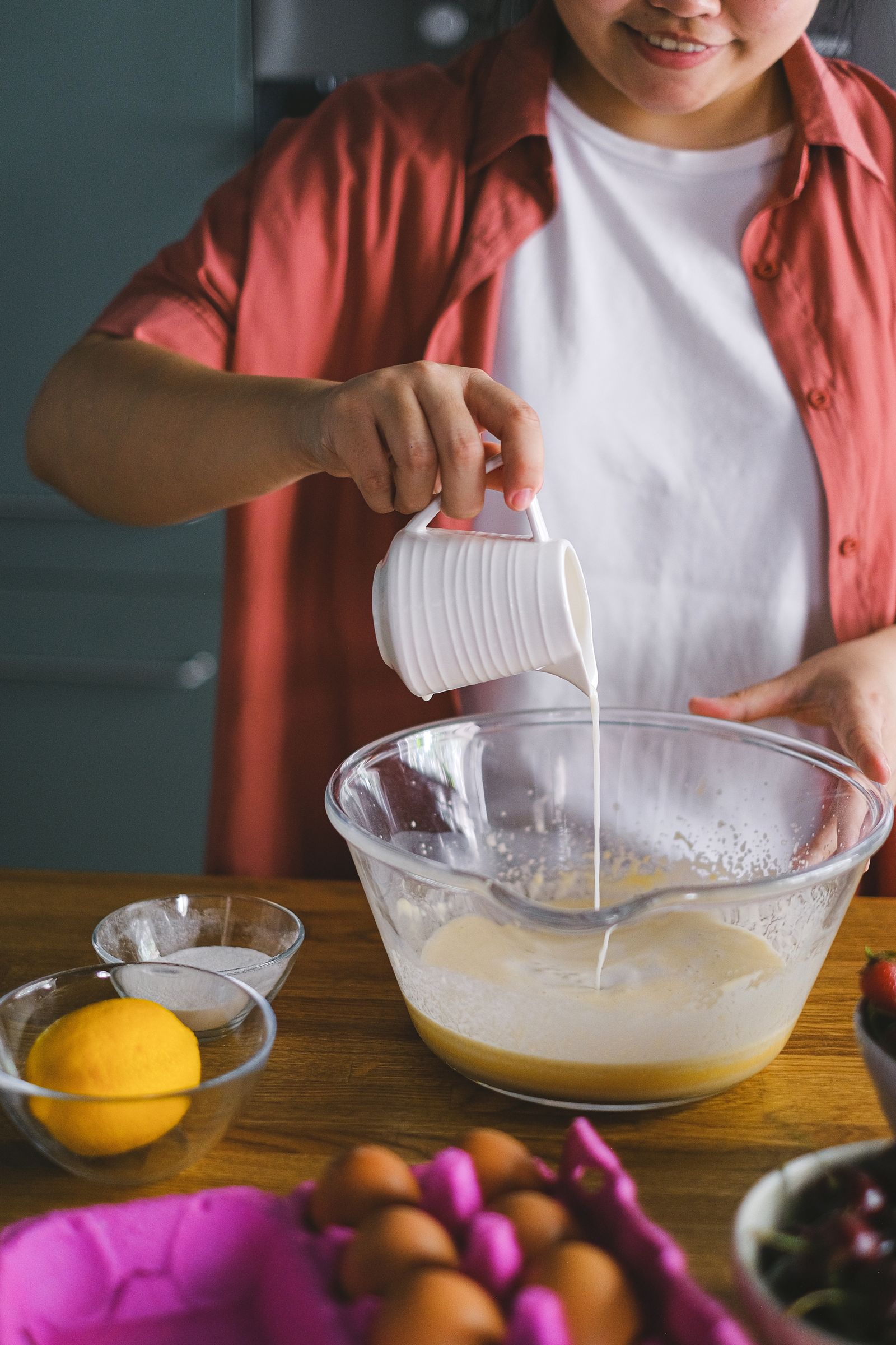 A person pouring milk from a striped mug into a glass bowl