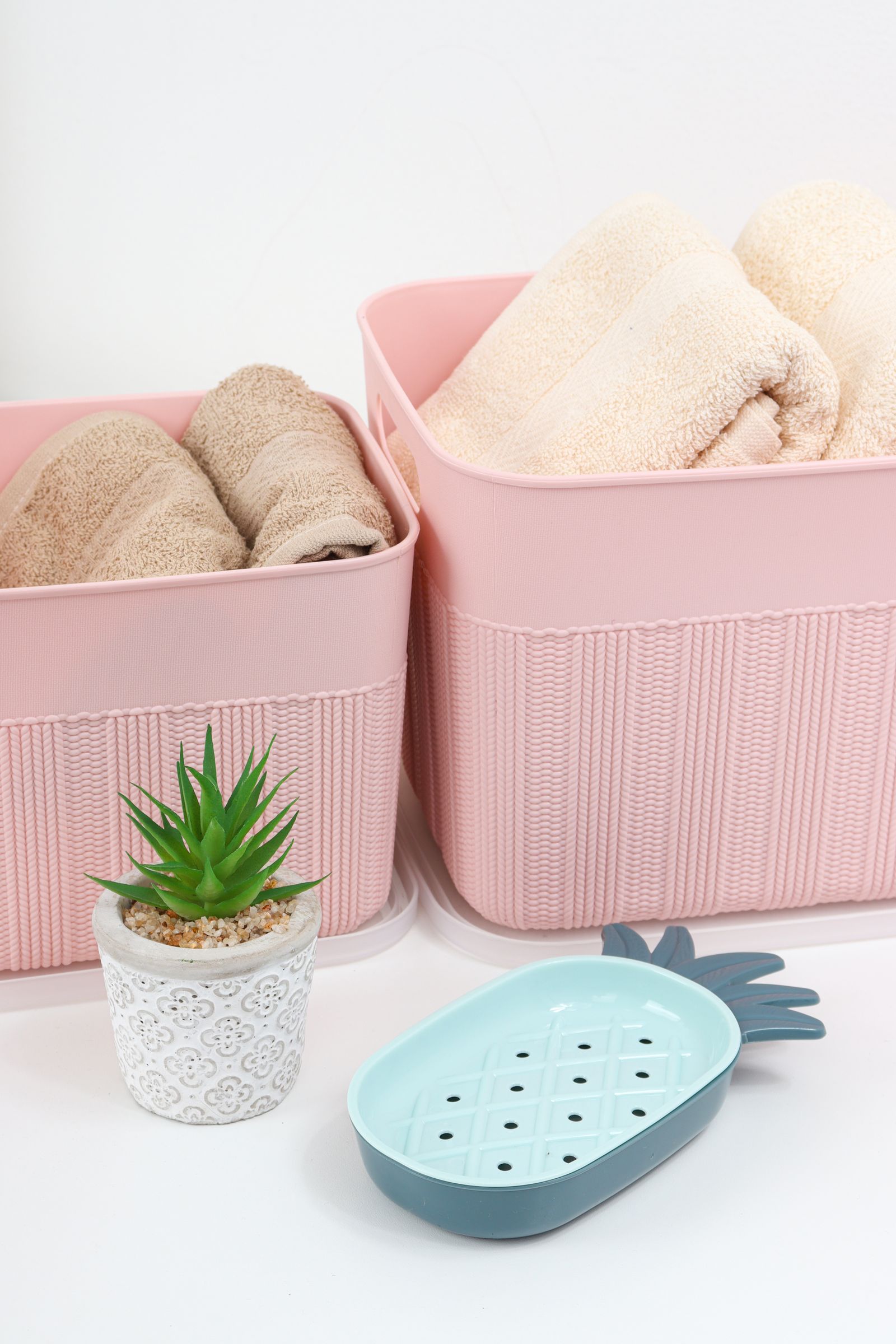 Rolled towels in pink baskets beside a plant and soap tray