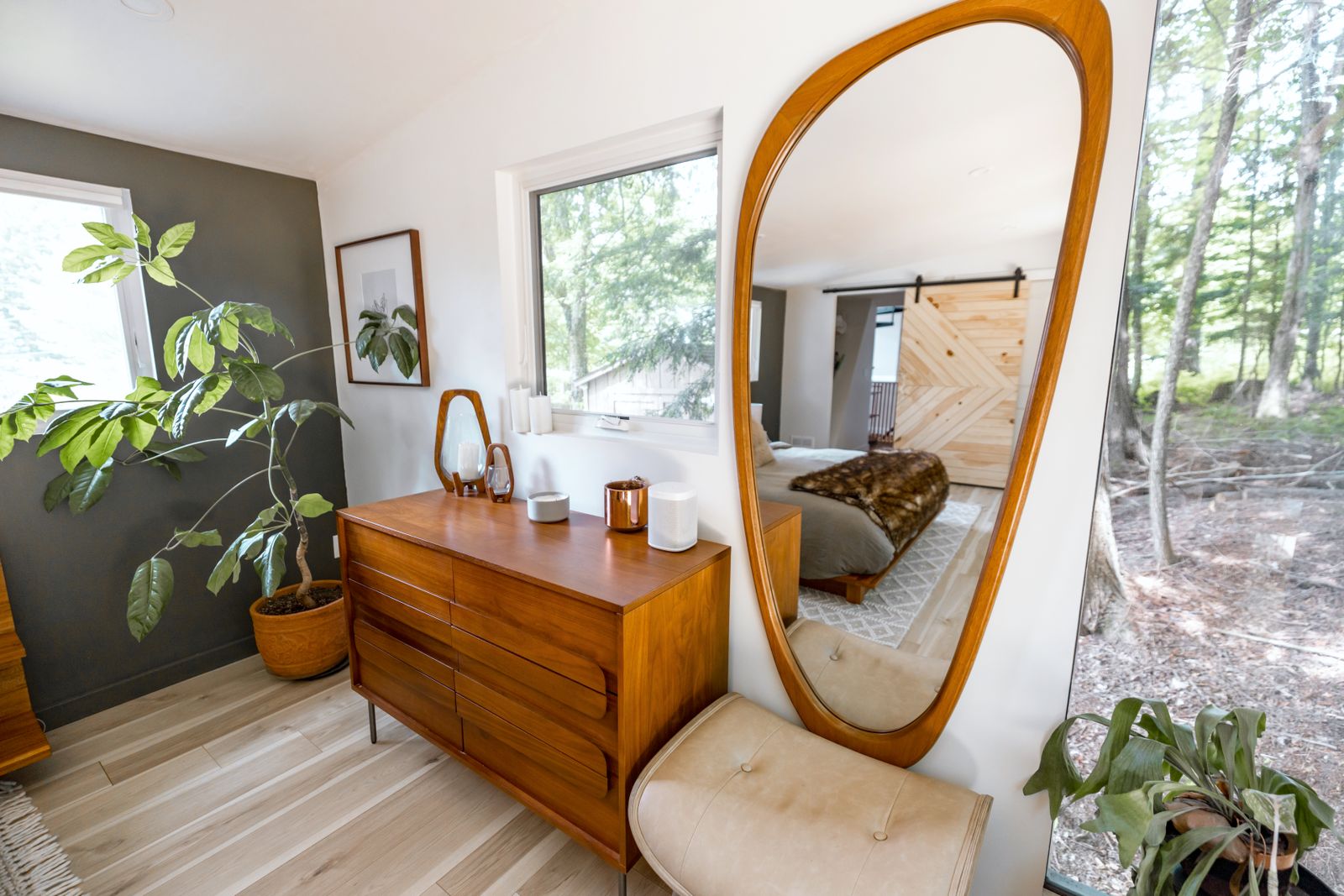 An oval mirror beside a wooden dresser and indoor plants