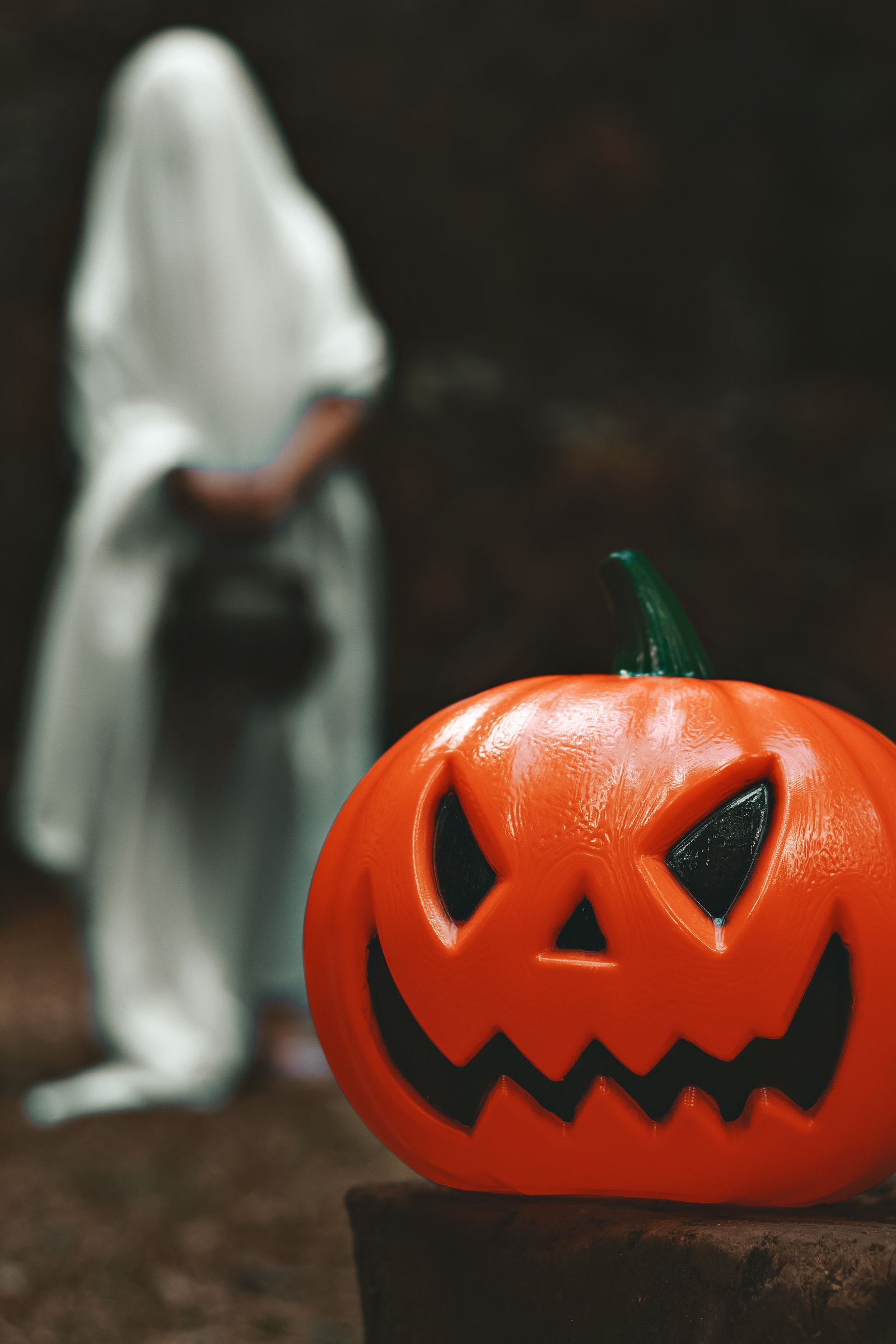 A carved pumpkin with a ghost figure behind it