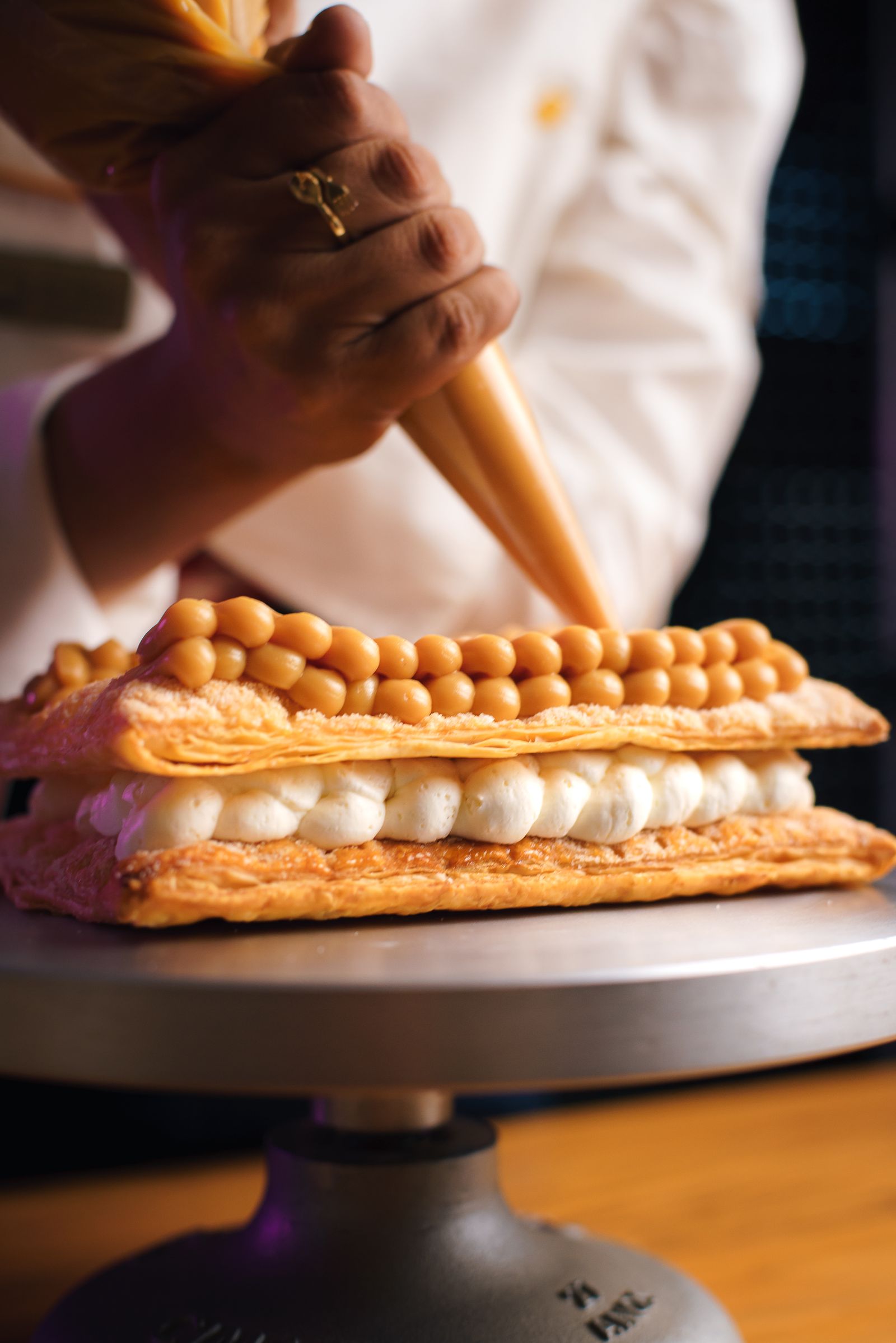 A baker piping cream onto a layered pastry