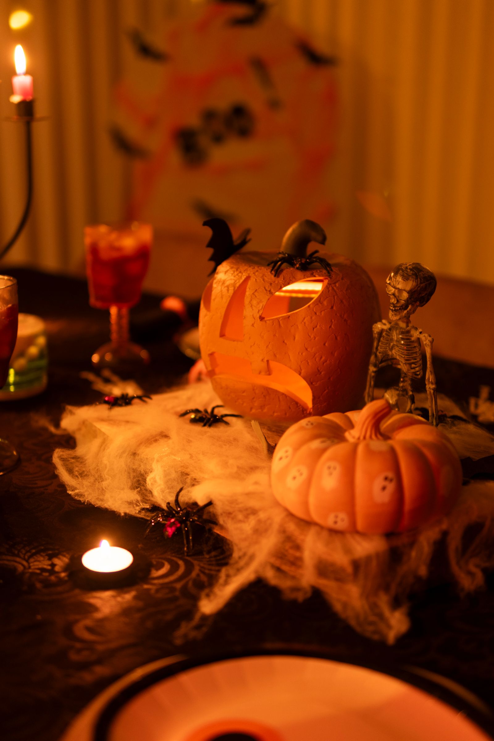 Jack-o-lanterns, skeleton decorations, and burning candles on a table
