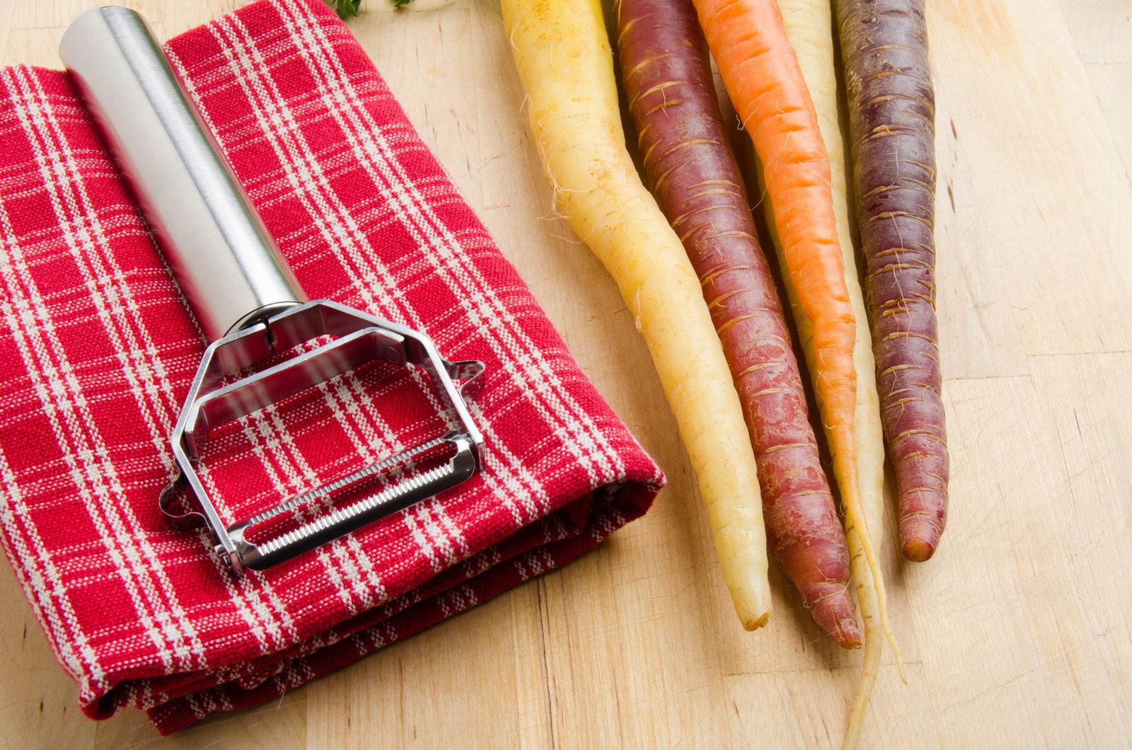 Carrots and a metal peeler beside a red checked cloth