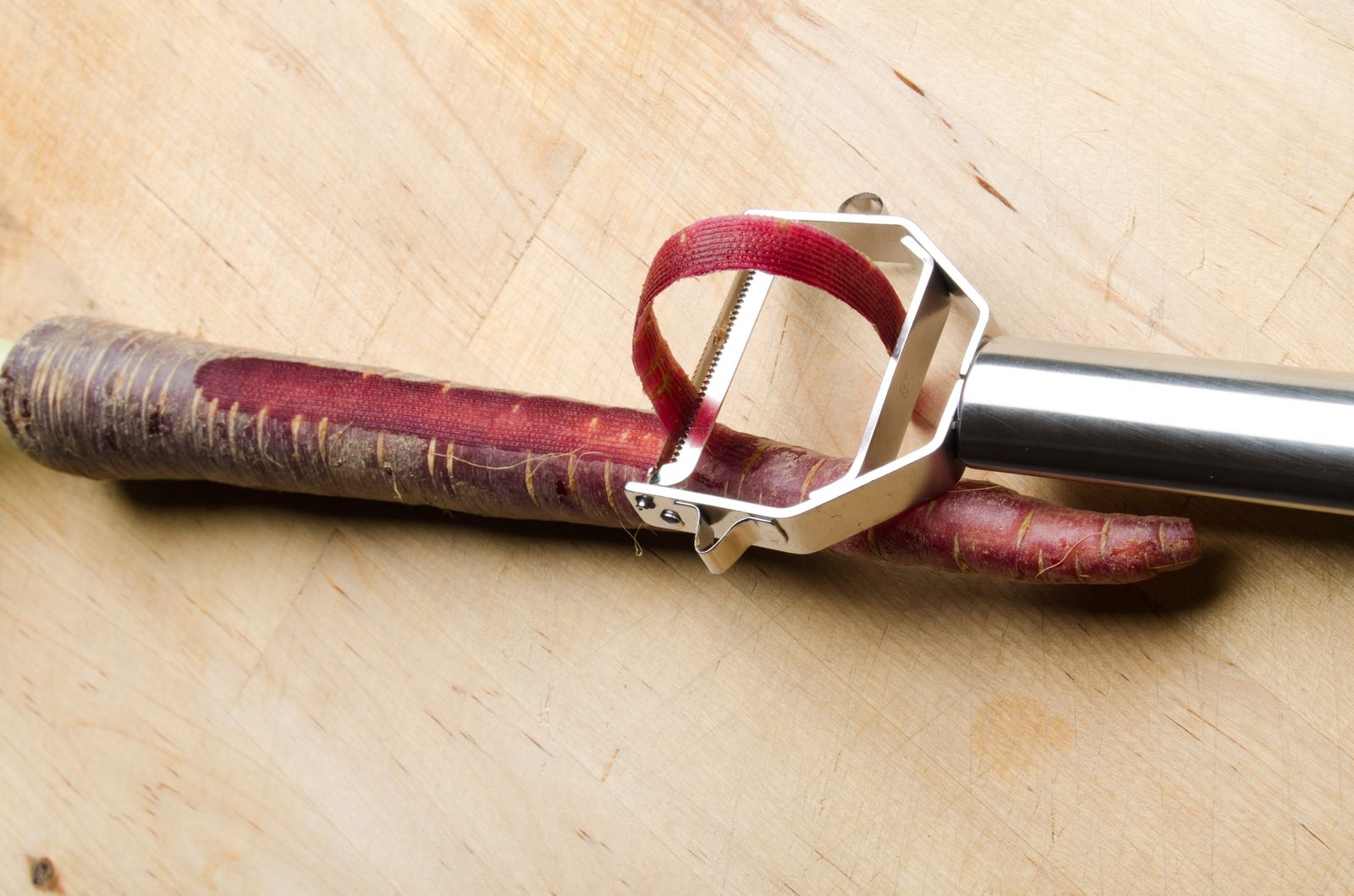 A purple carrot and a metal Y-shaped peeler on a board