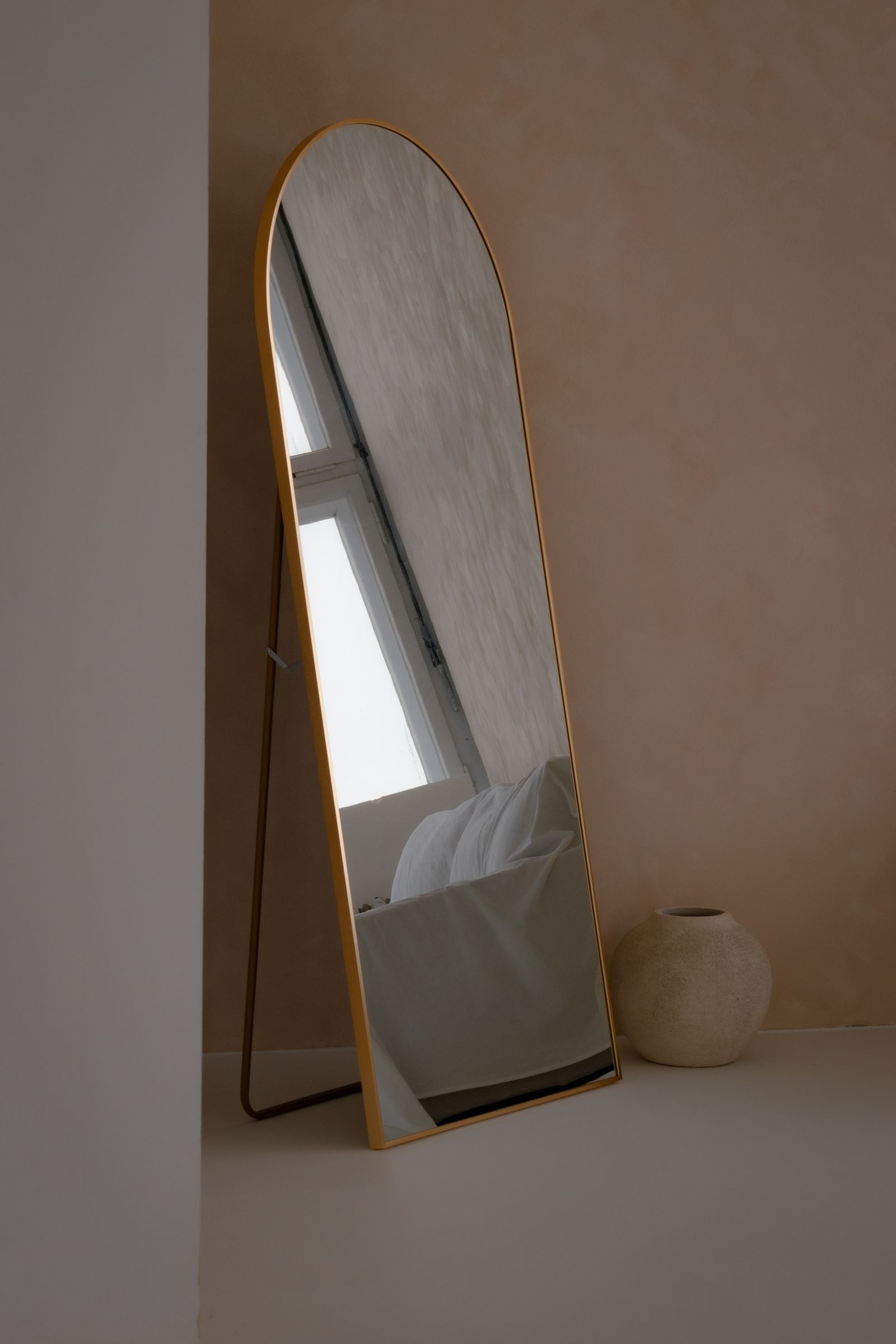 A tall rounded mirror leaning in an interior corner