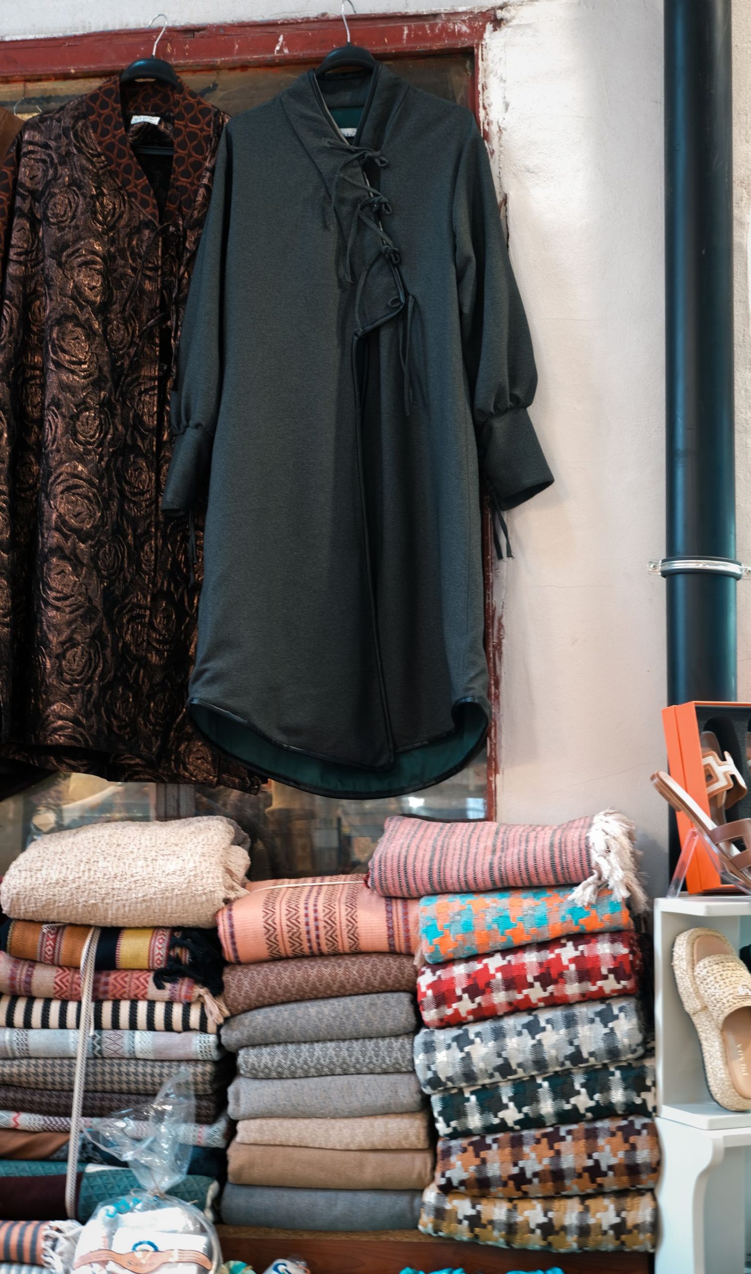 Folded patterned scarves below hanging garments in a shop