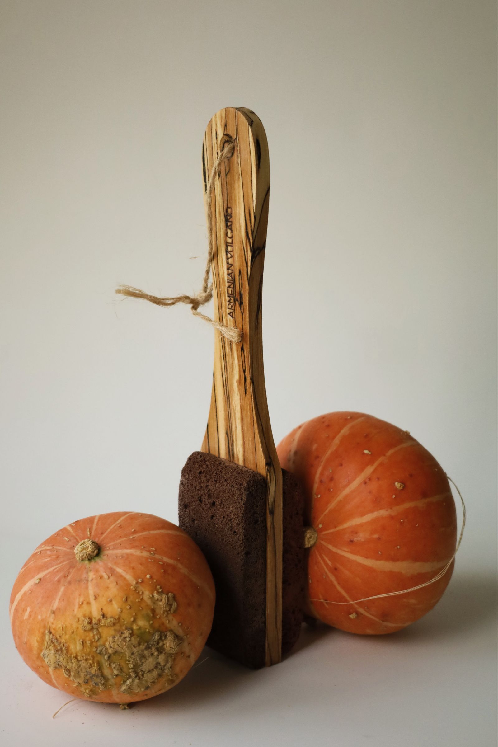 Two pumpkins and a wooden brush against a neutral background
