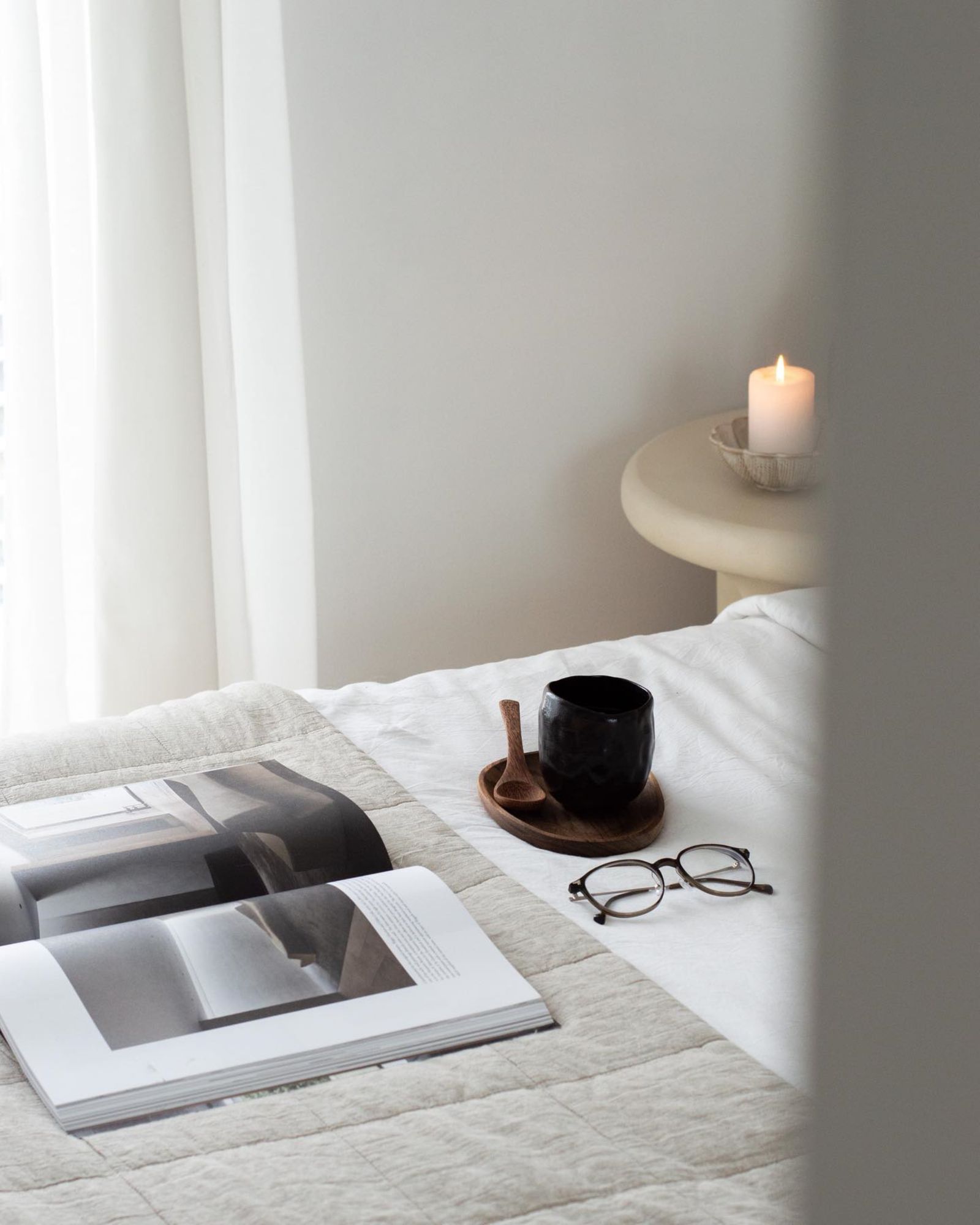 Glasses and a mug beside an open book on a bed