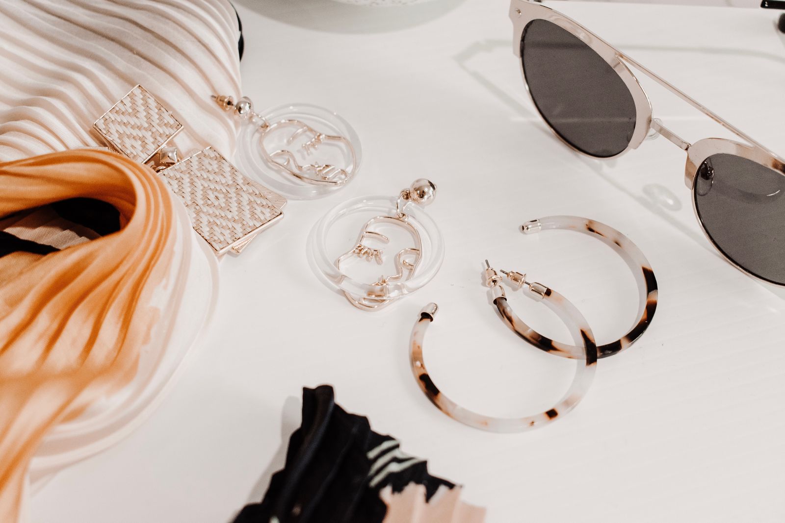 A patterned scarf beside earrings and sunglasses