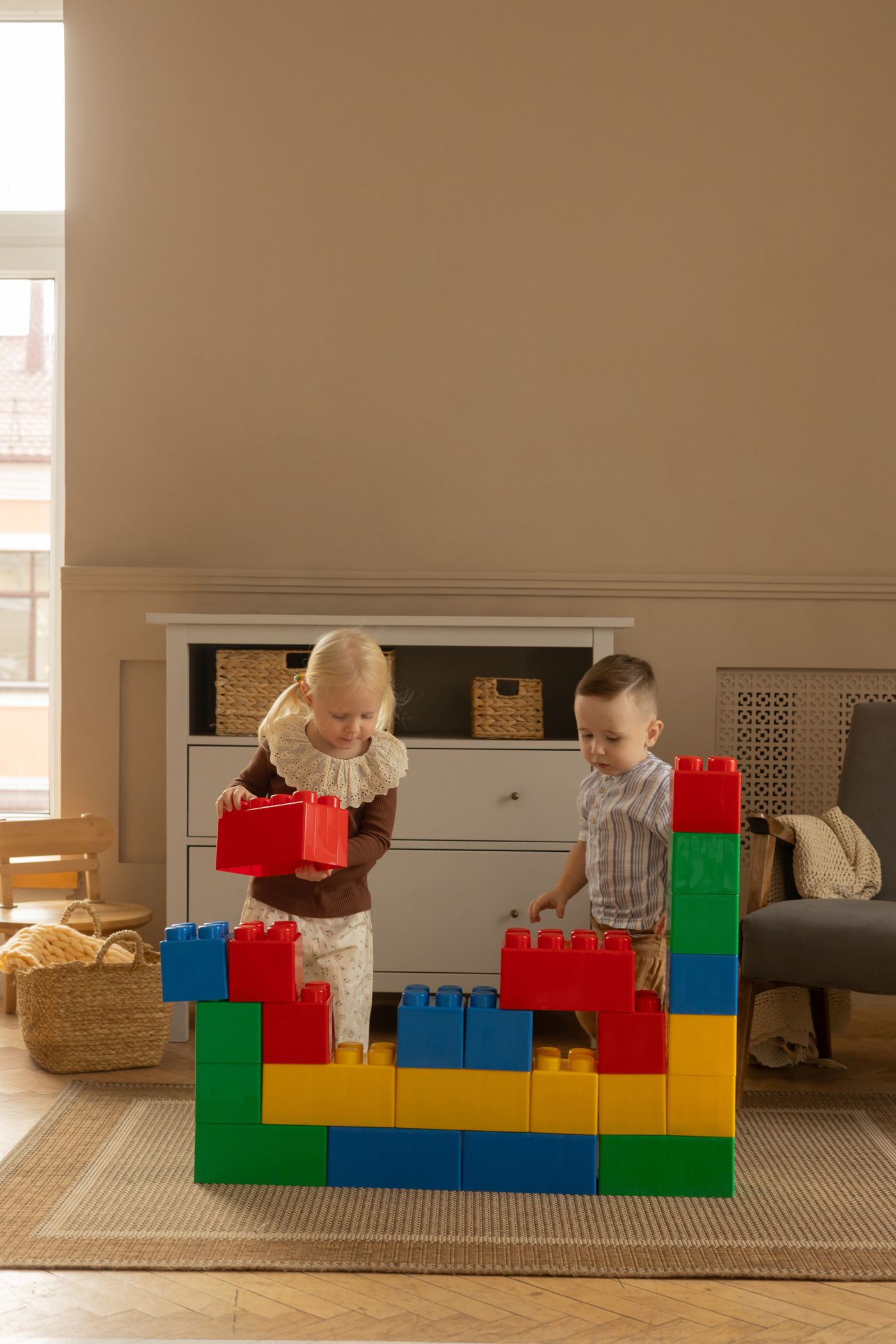 Two children assembling large blocks beside a fireplace