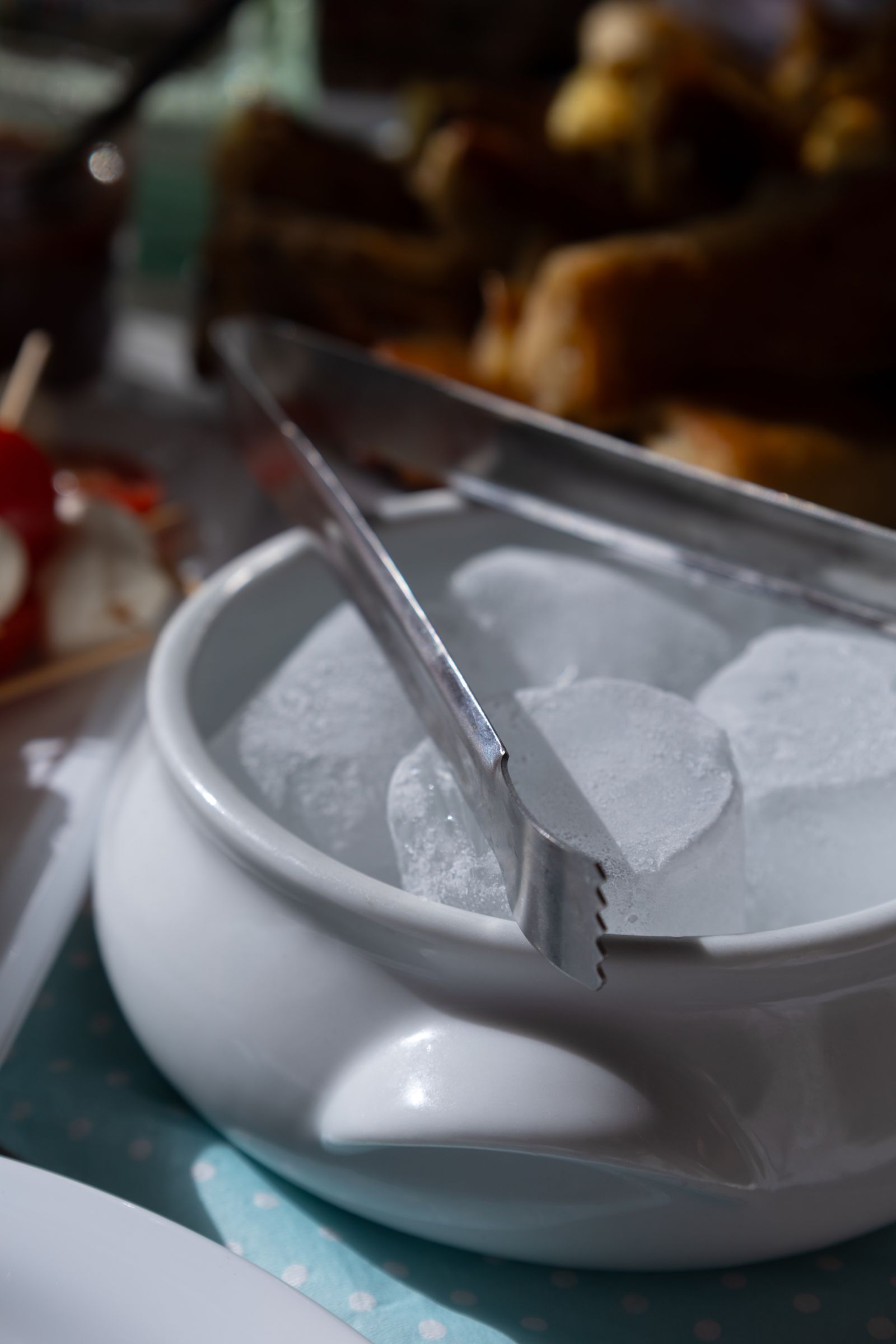 Ice cubes and serving tongs in a pale bowl