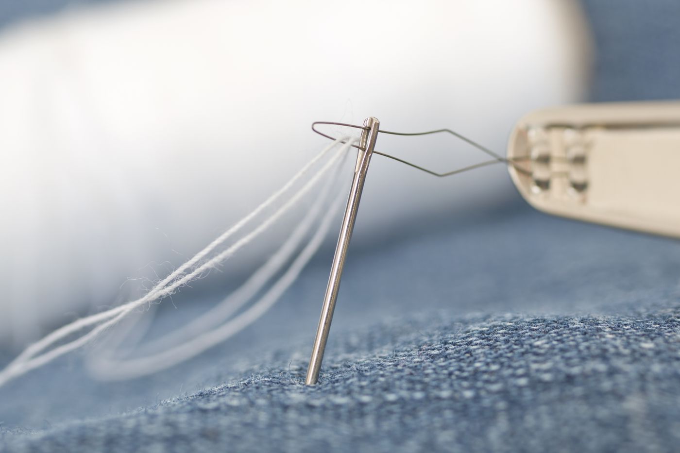 Threaded needle resting on fabric near a thimble