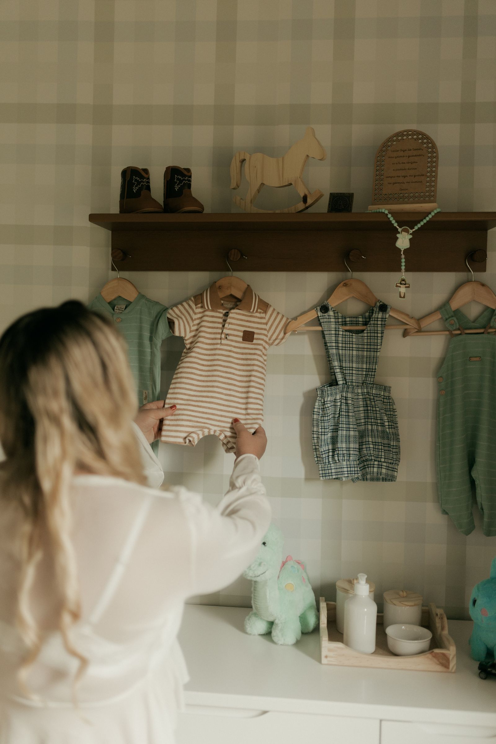 An adult selecting child clothing from a nursery shelf