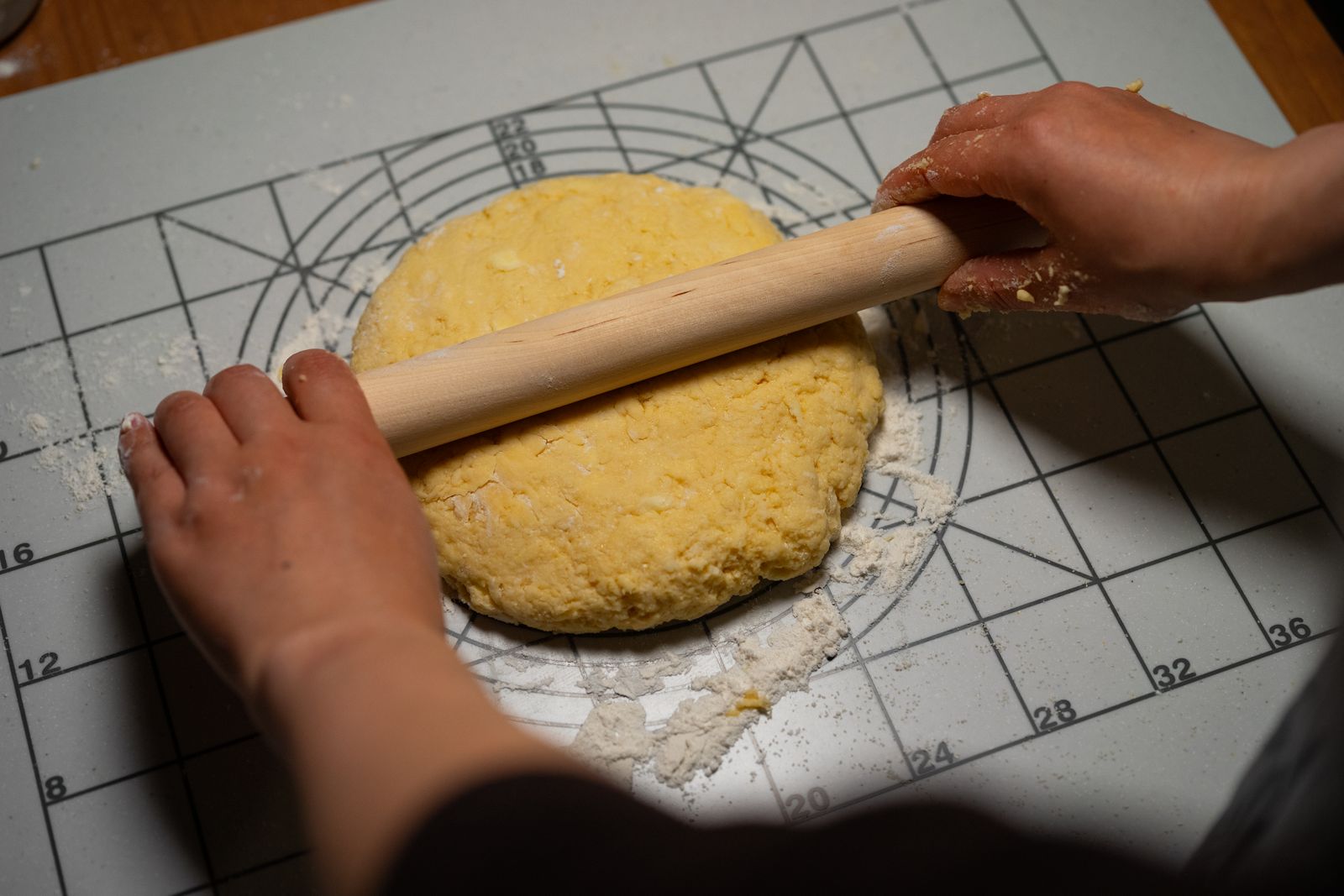 Hands rolling dough on a marked preparation mat