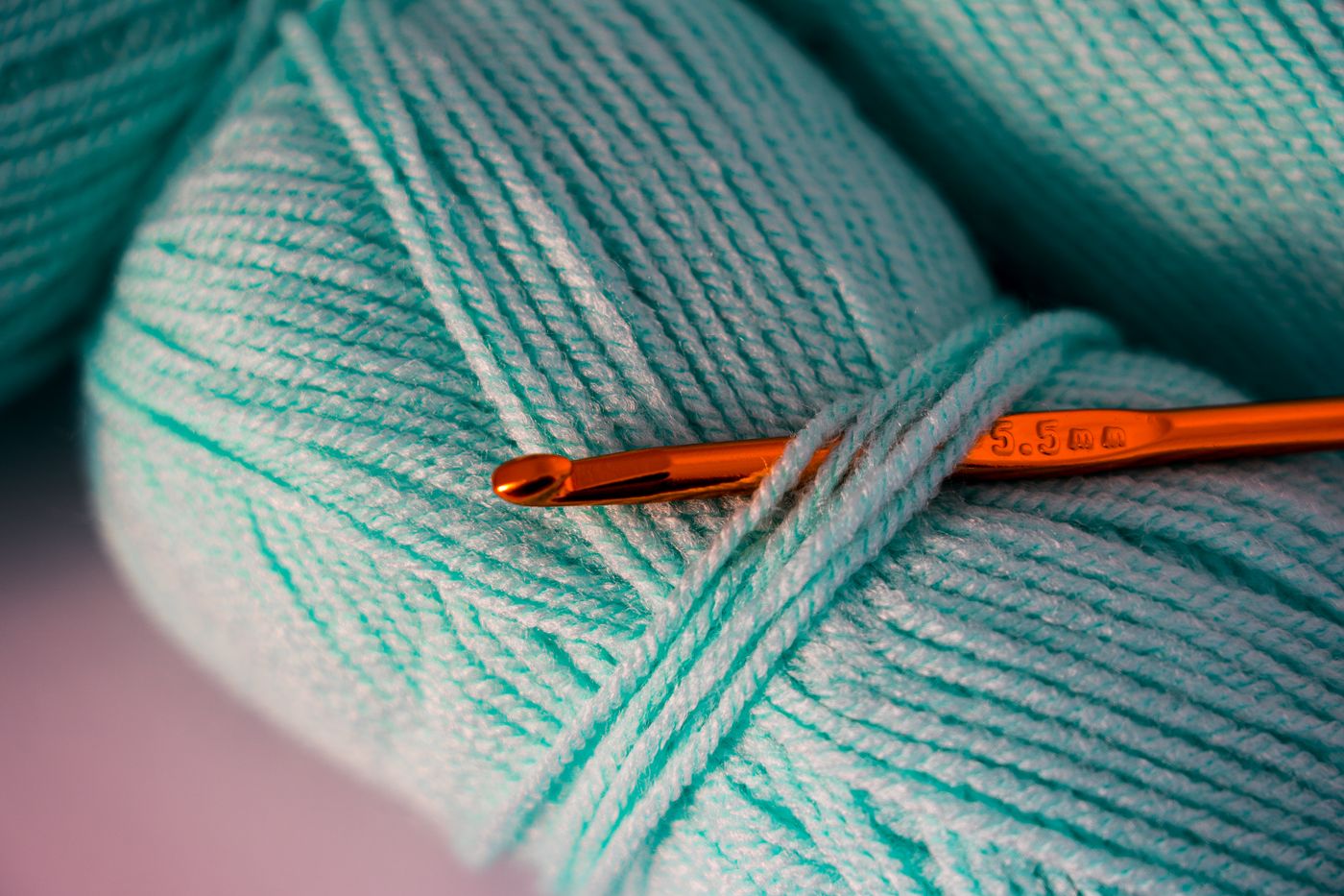 A crochet hook resting beside teal yarn