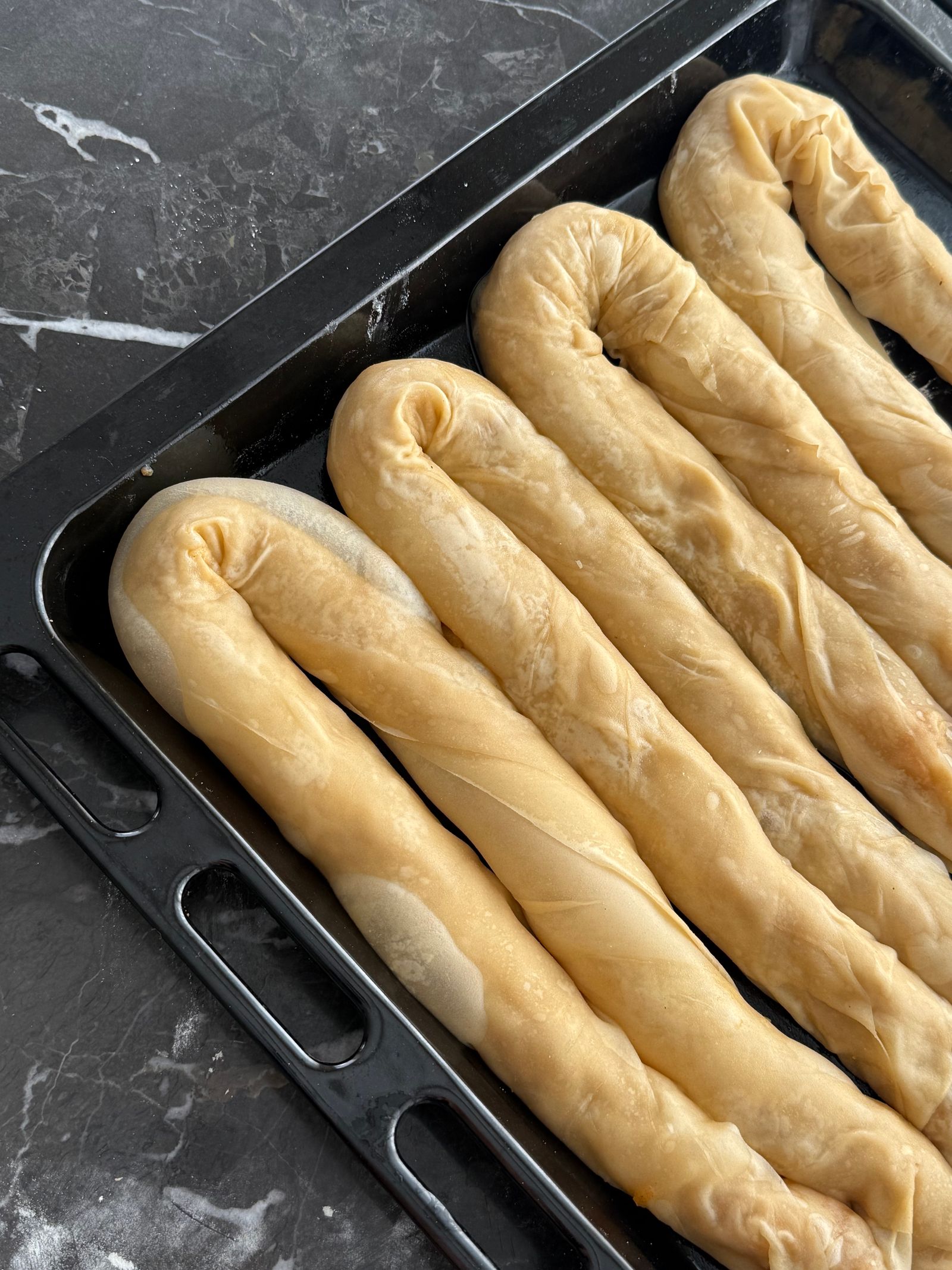 Raw dough rolls arranged in a dark rimmed baking tray
