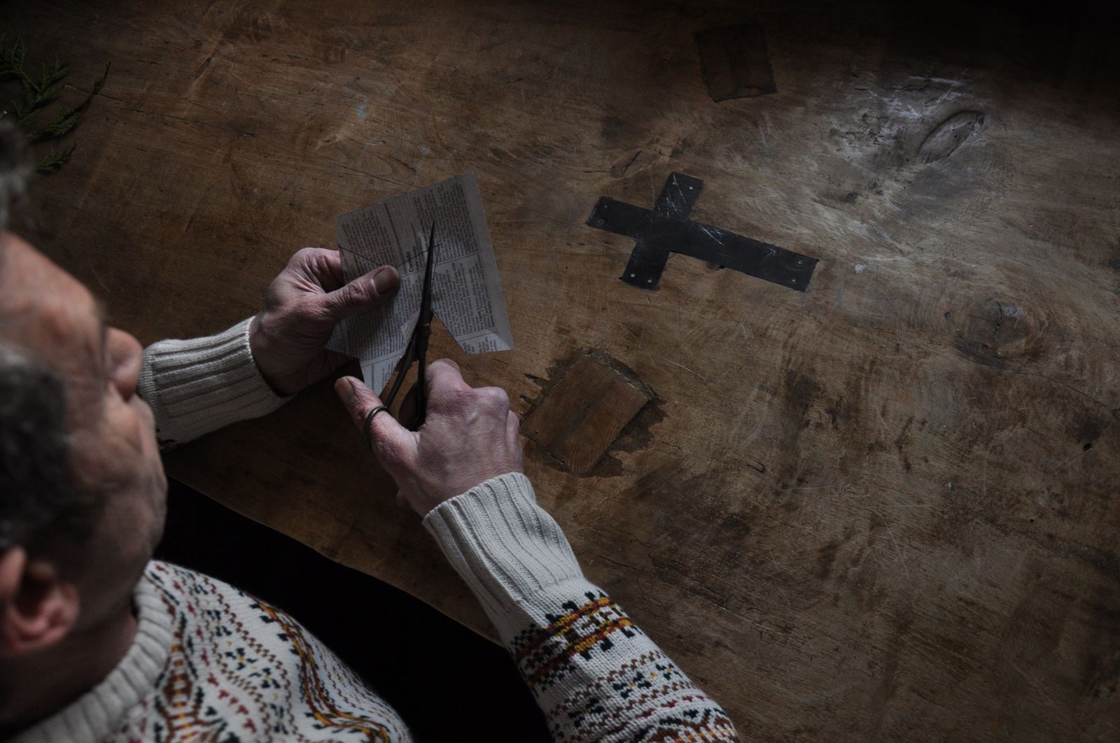 Hands cutting a small paper piece at a dark wooden table