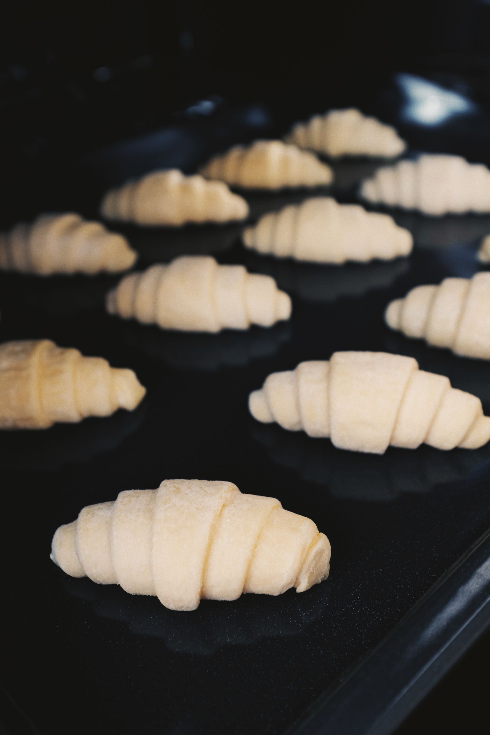 Raw croissant dough arranged on a dark baking tray