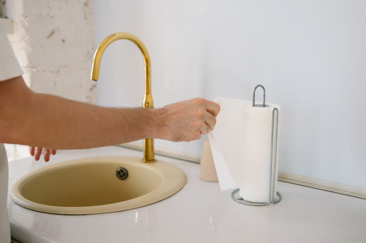 A paper towel held beside a modern gold-colored faucet