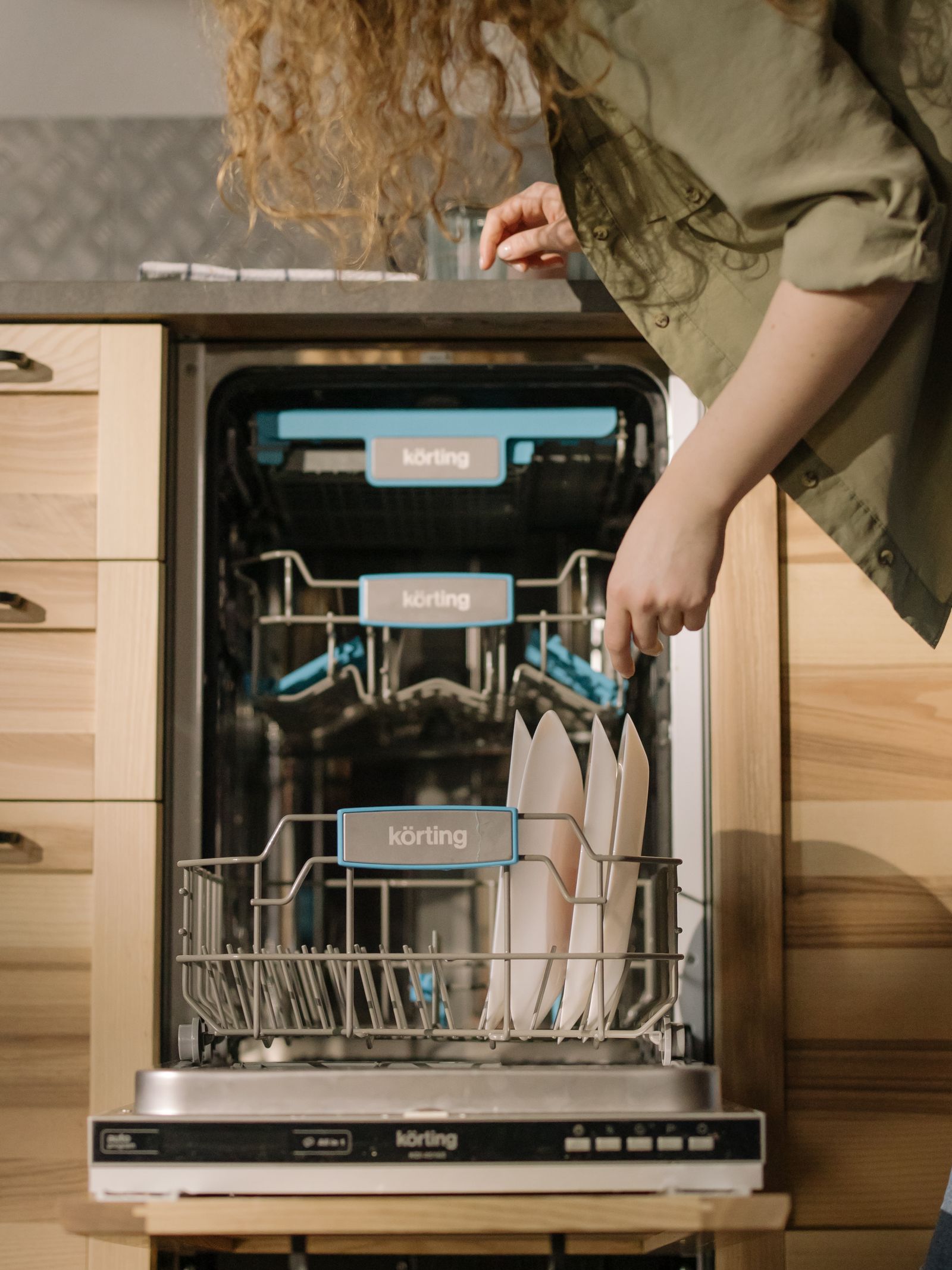 A person loading an open dishwasher in a kitchen