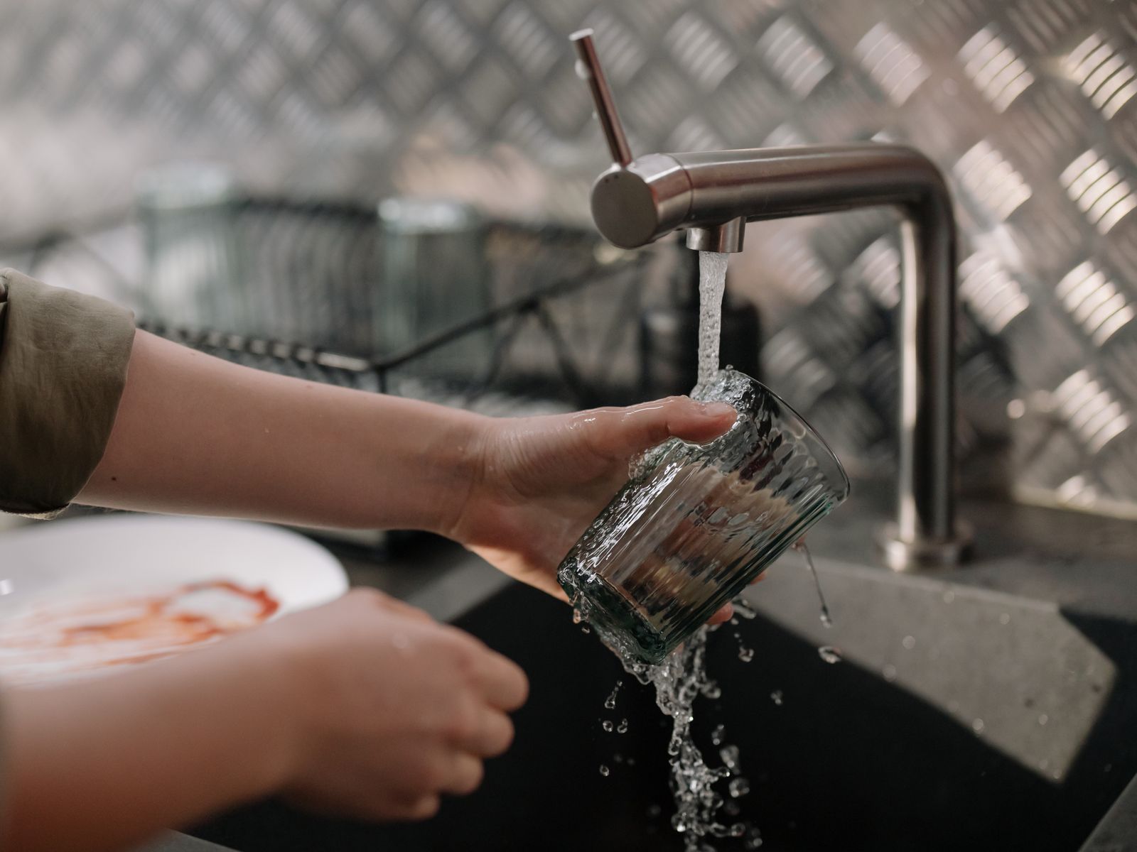 Hands rinsing a drinking glass under a kitchen faucet