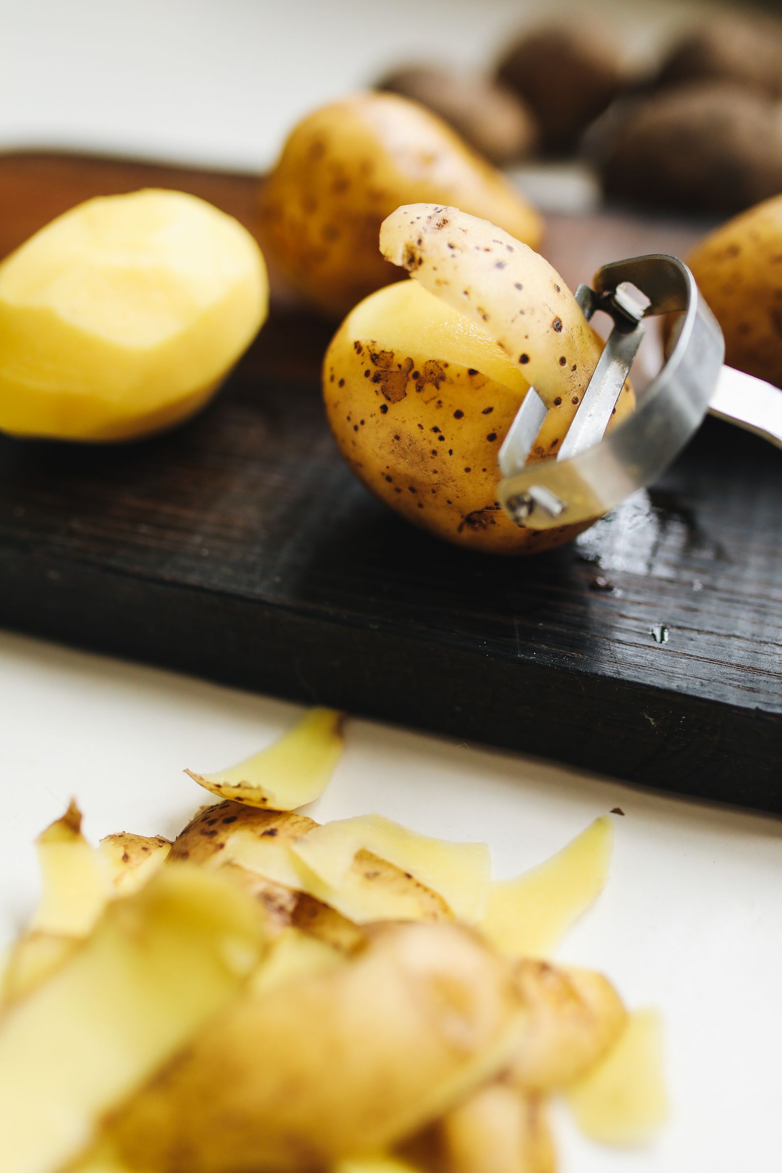 A potato, peeler, and peelings on a dark preparation surface