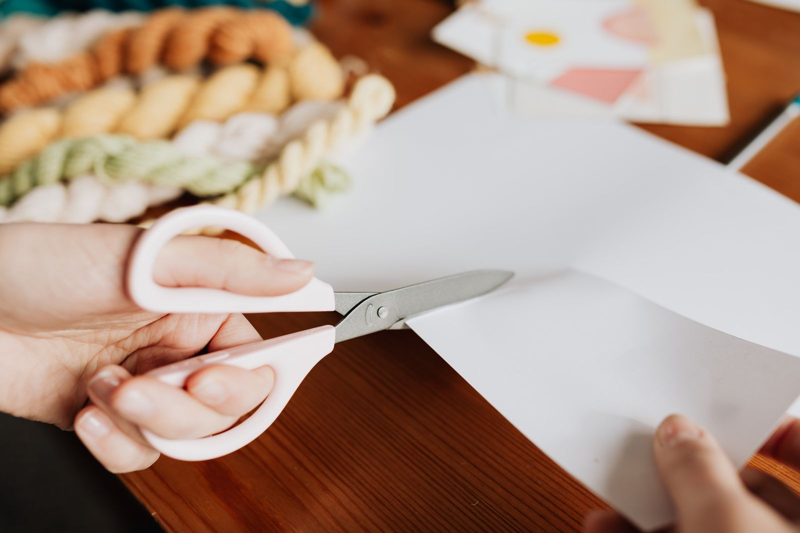 Hands cutting a paper sheet with white and pink scissors