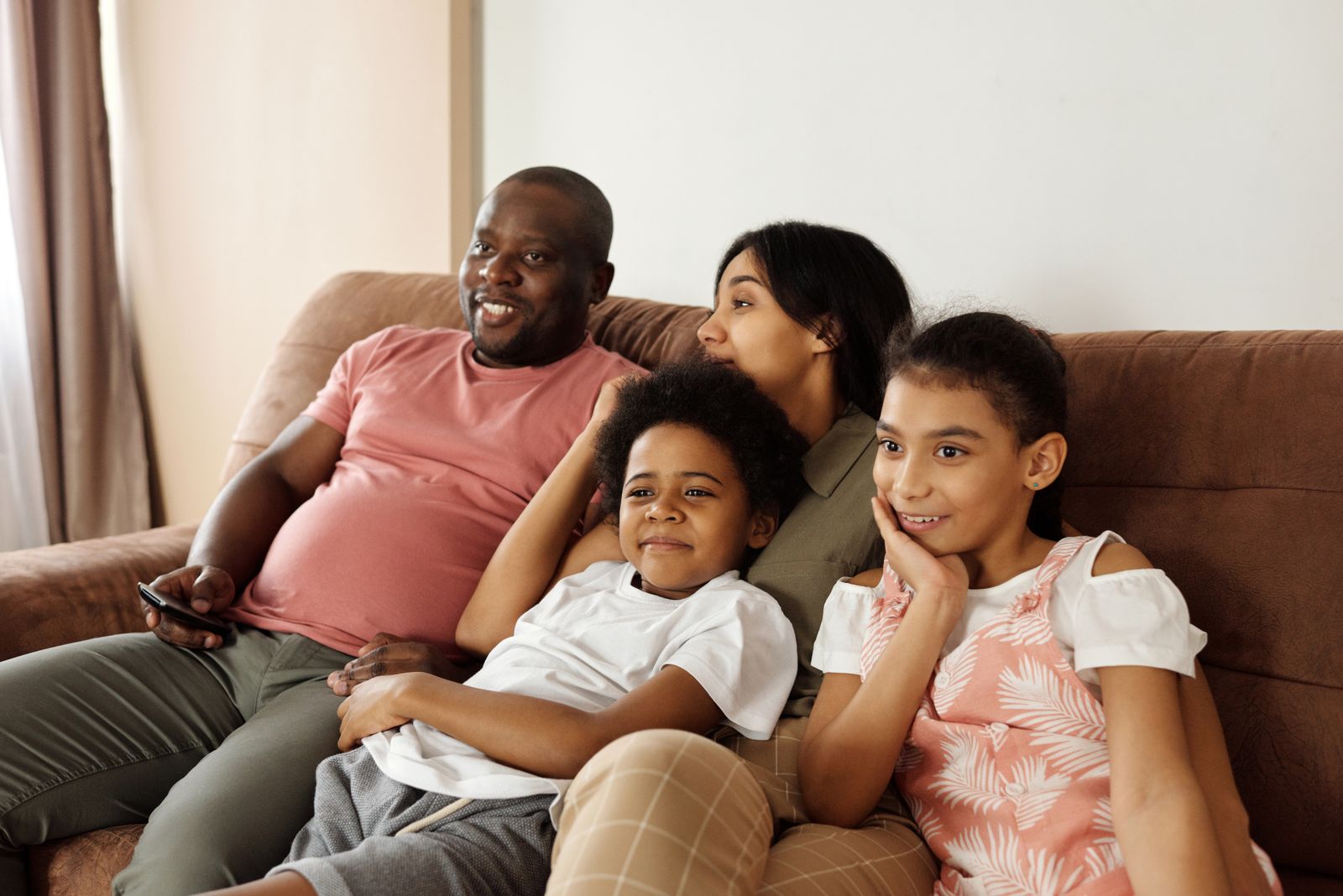 A family of four seated together on a brown sofa
