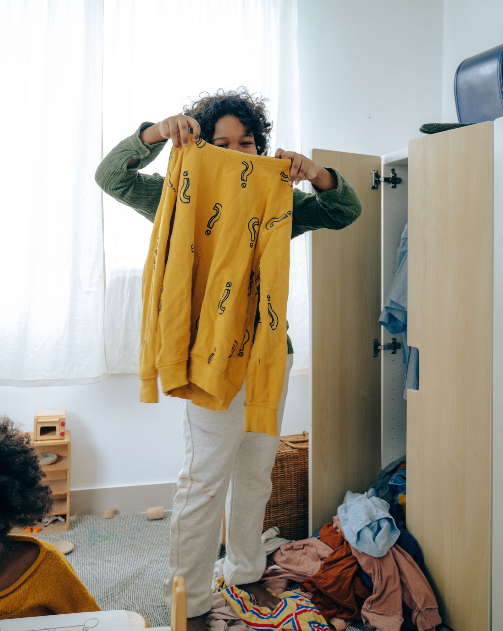 A child holding a yellow garment near bedroom clothing storage