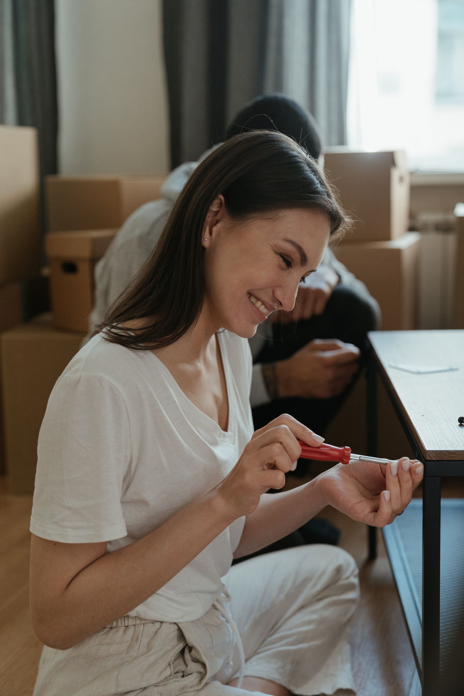 Two people using a tool while assembling furniture near moving boxes