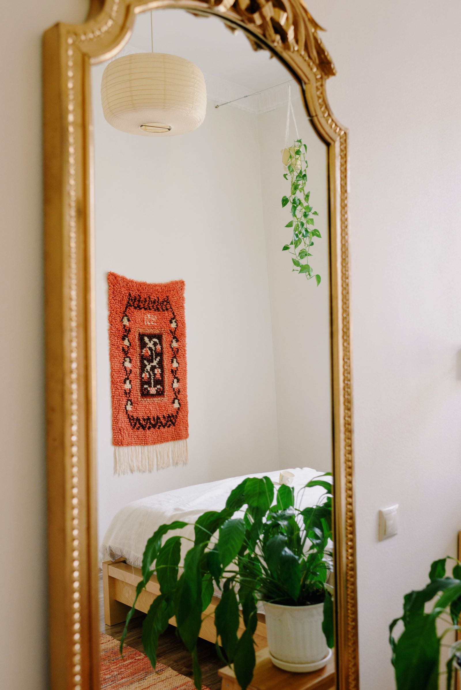 A gold-framed mirror reflecting plants and bedroom furnishings