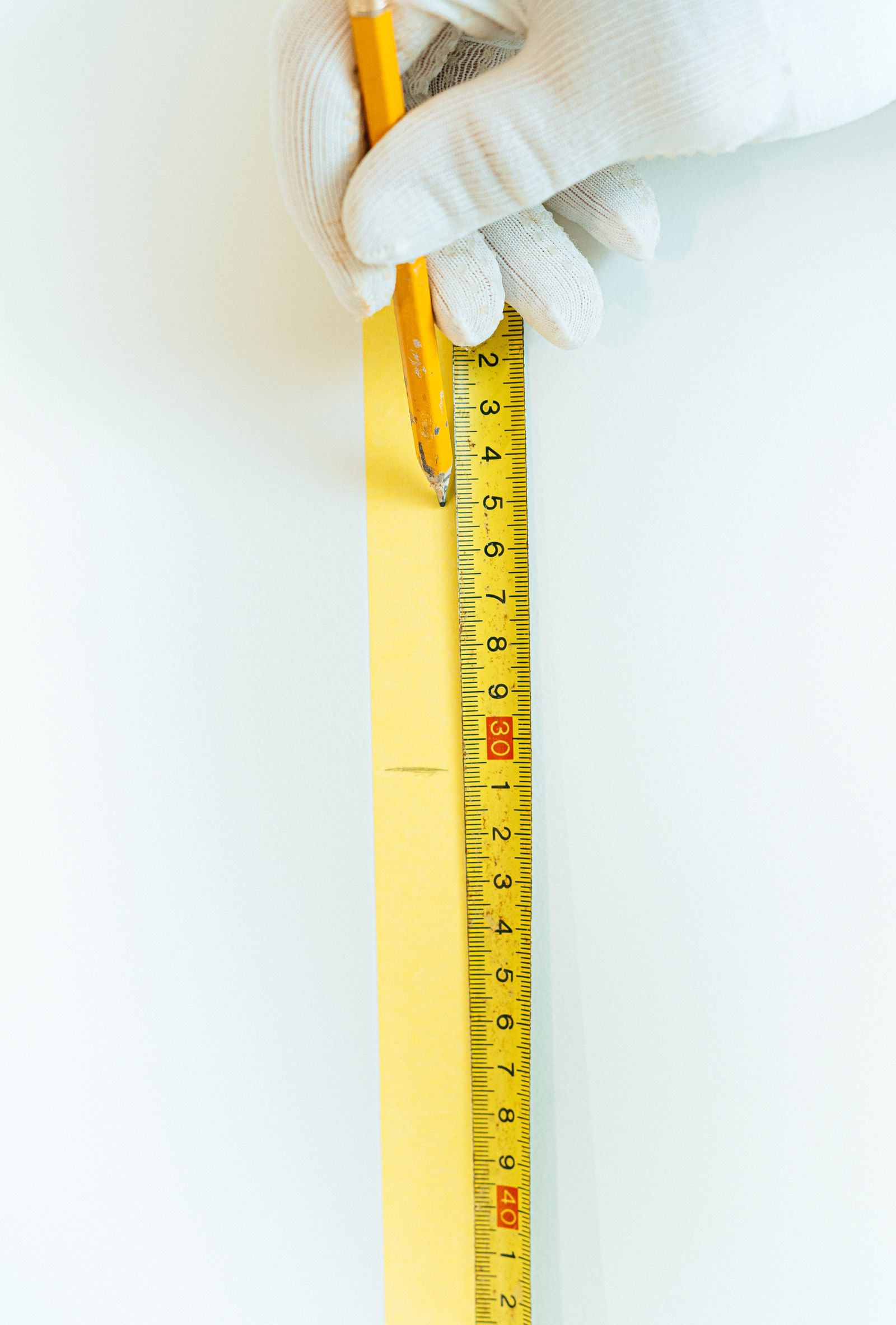 A gloved hand holding a pencil beside a tape measure