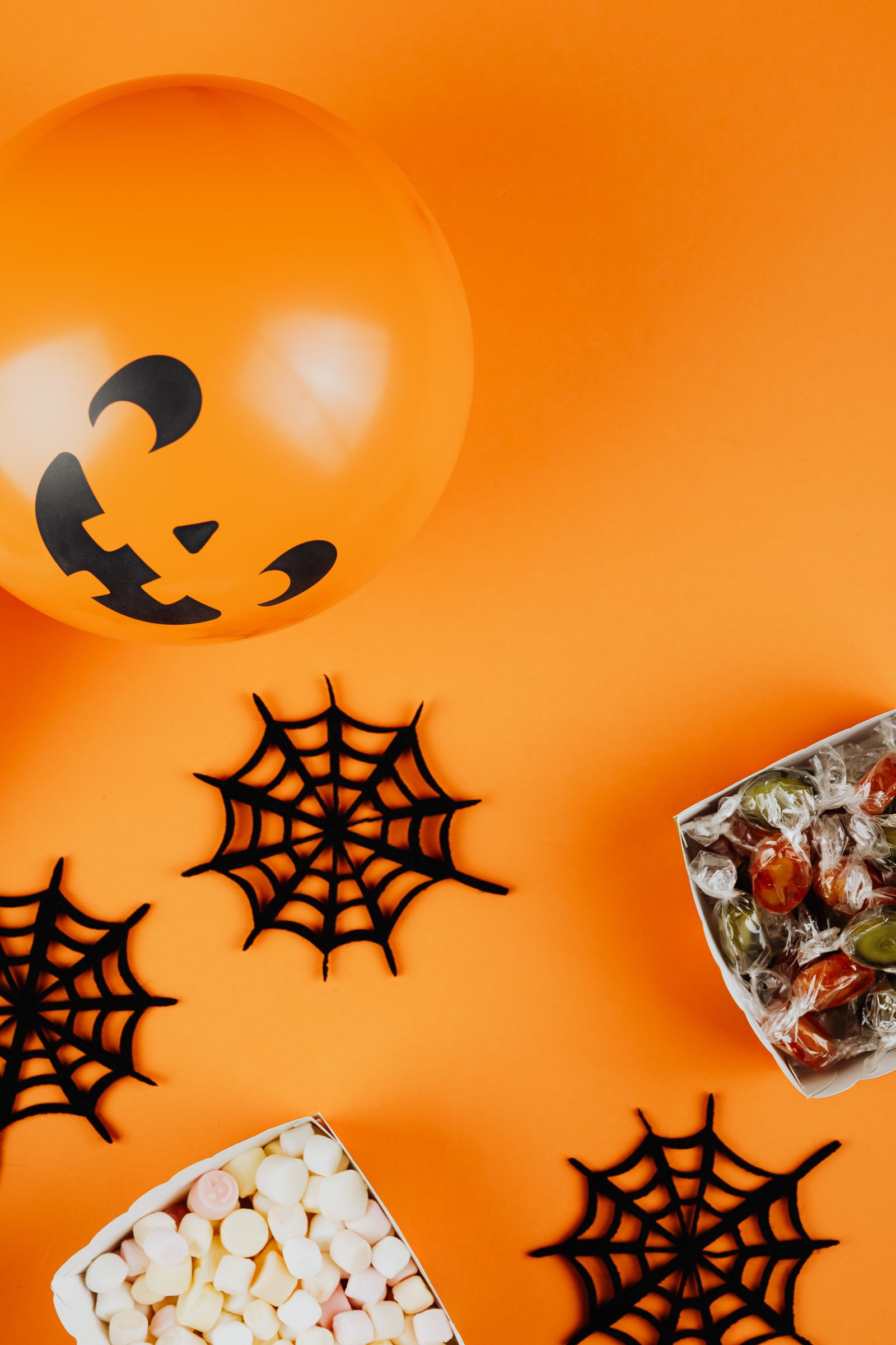 Paper cobwebs, a Halloween balloon, and sweets on an orange surface