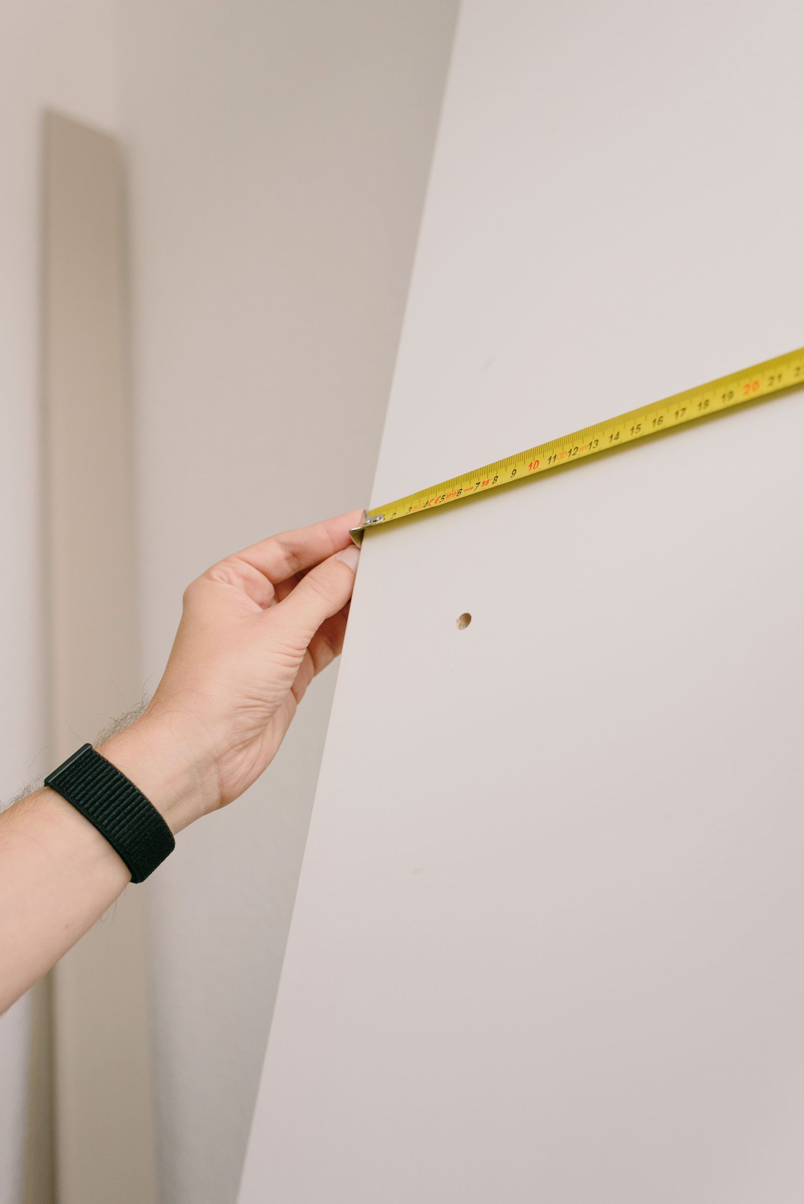 A hand holding a measuring tape against a pale wall