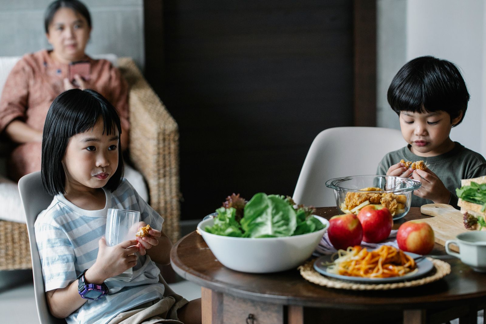 Children eating at a table with an adult nearby