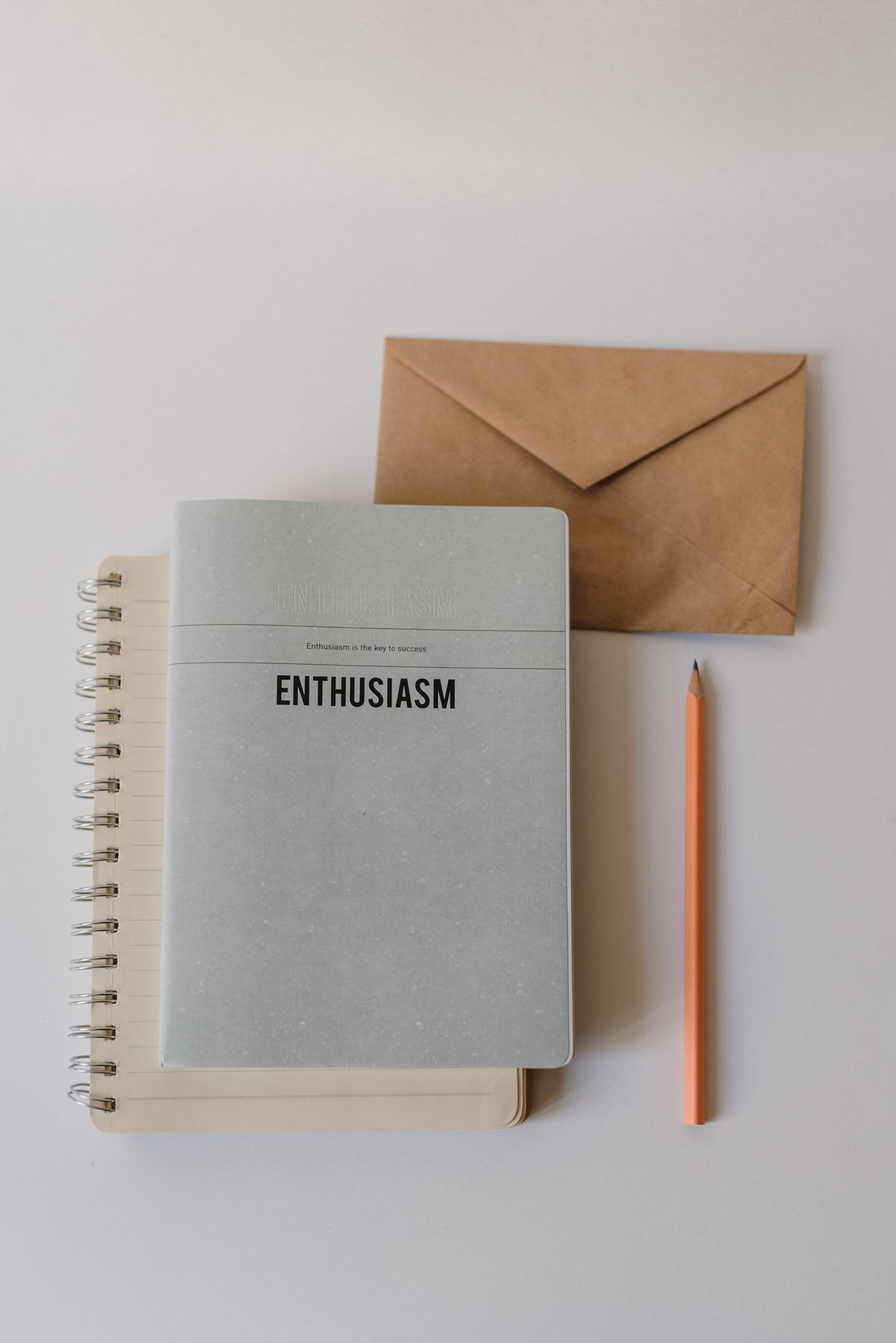 A notebook, envelope, pencil, and pen arranged on a pale surface