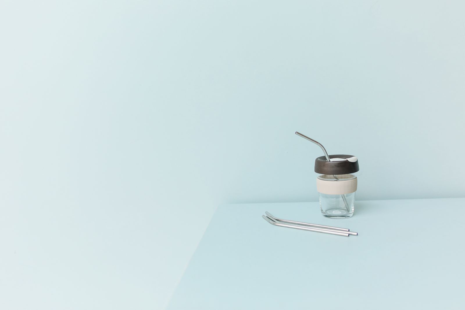 A reusable cup with a metal straw beside a loose straw on a blue surface