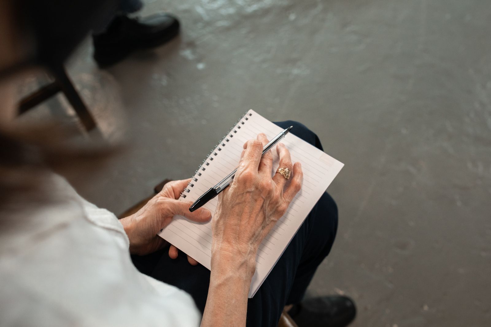 A seated person holding a pen and writing on a small paper pad