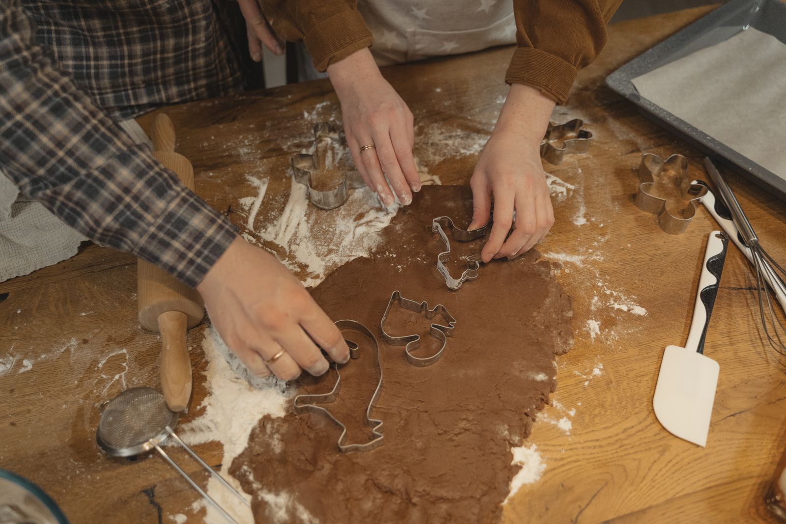 Two people cutting dough together at a wooden table
