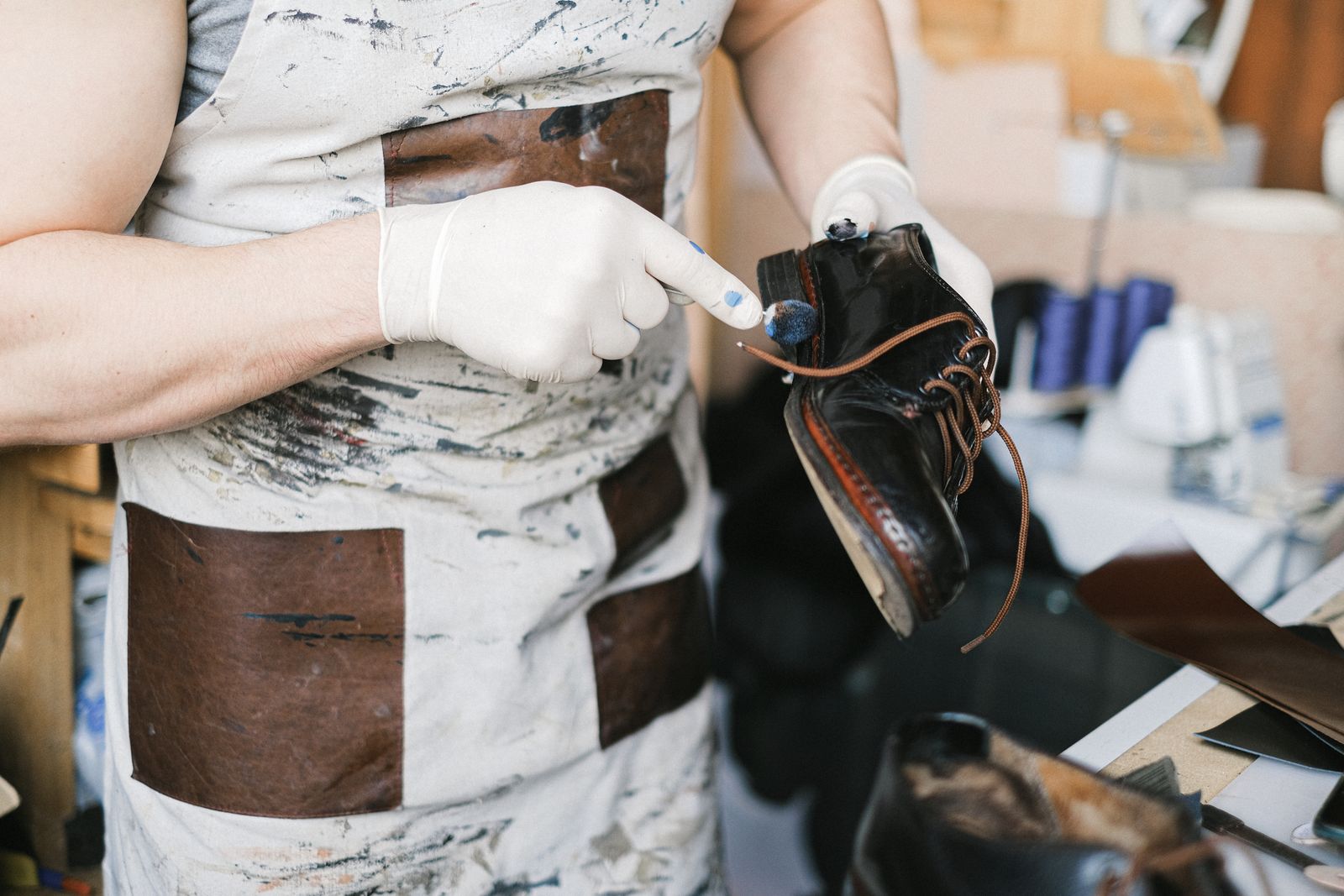 A gloved worker holding and treating a dark shoe