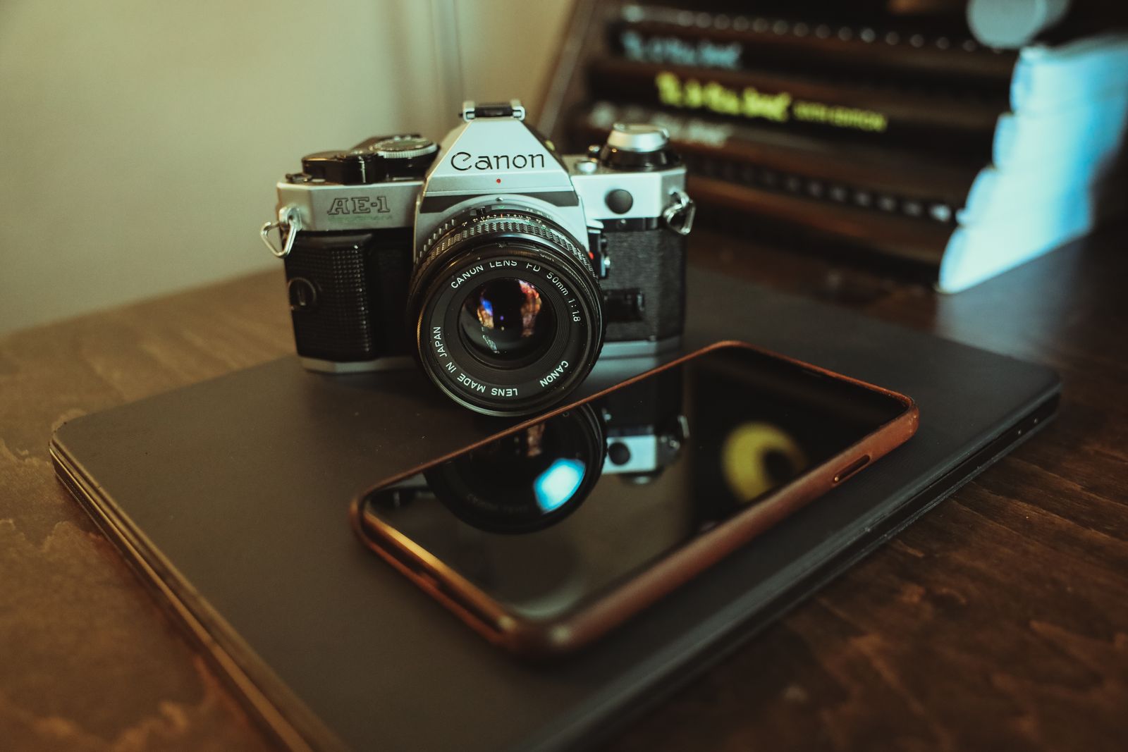 A camera and smartphone resting above a laptop on a wooden table