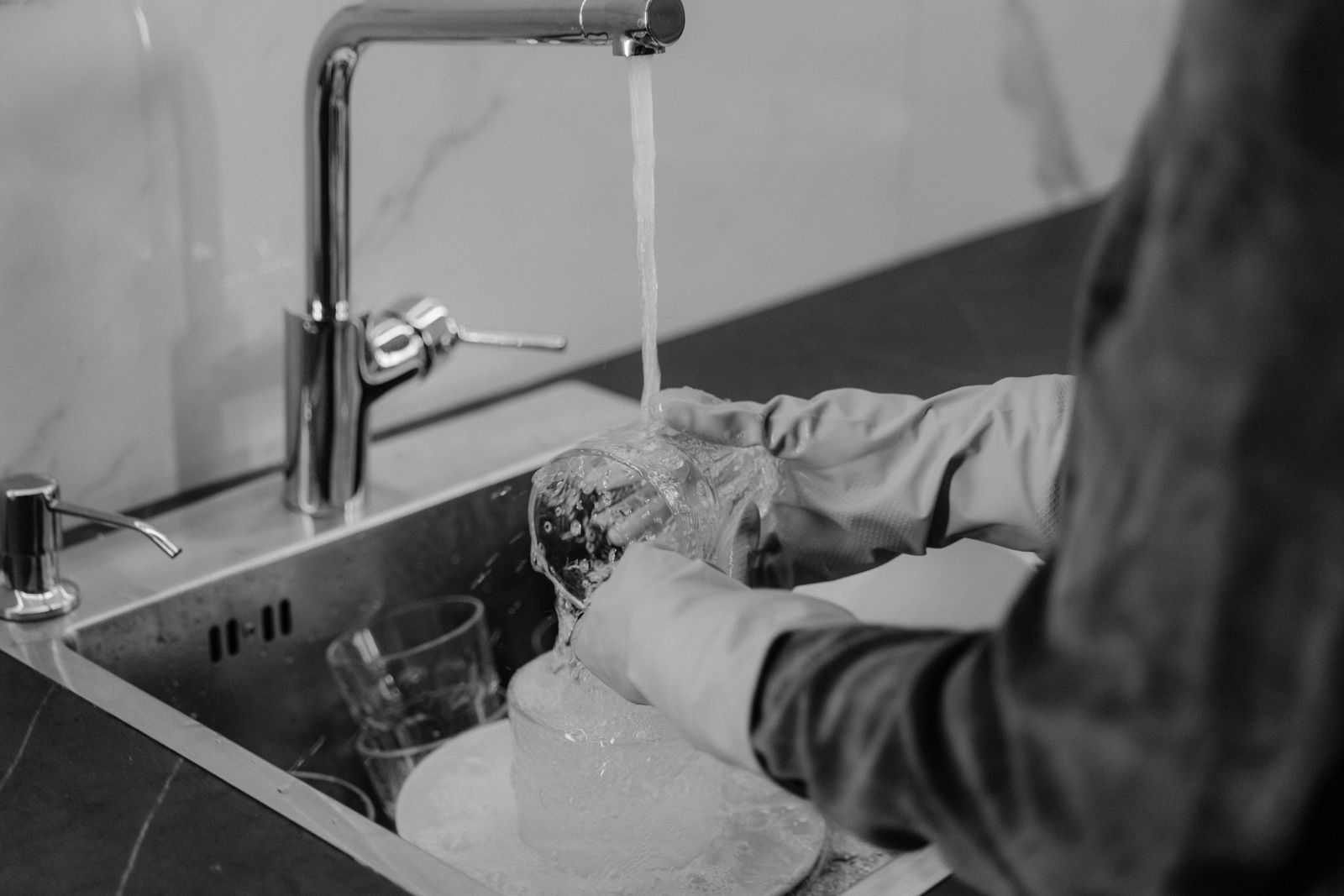 A person washing a glass at a kitchen sink in a monochrome photograph