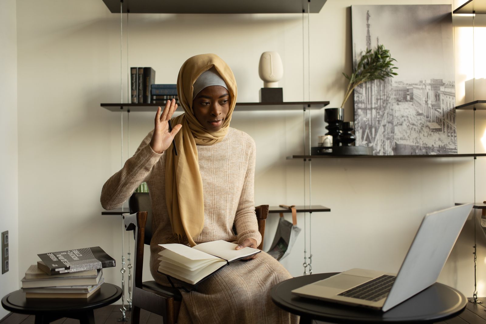 A person waving toward a laptop beside an open notebook