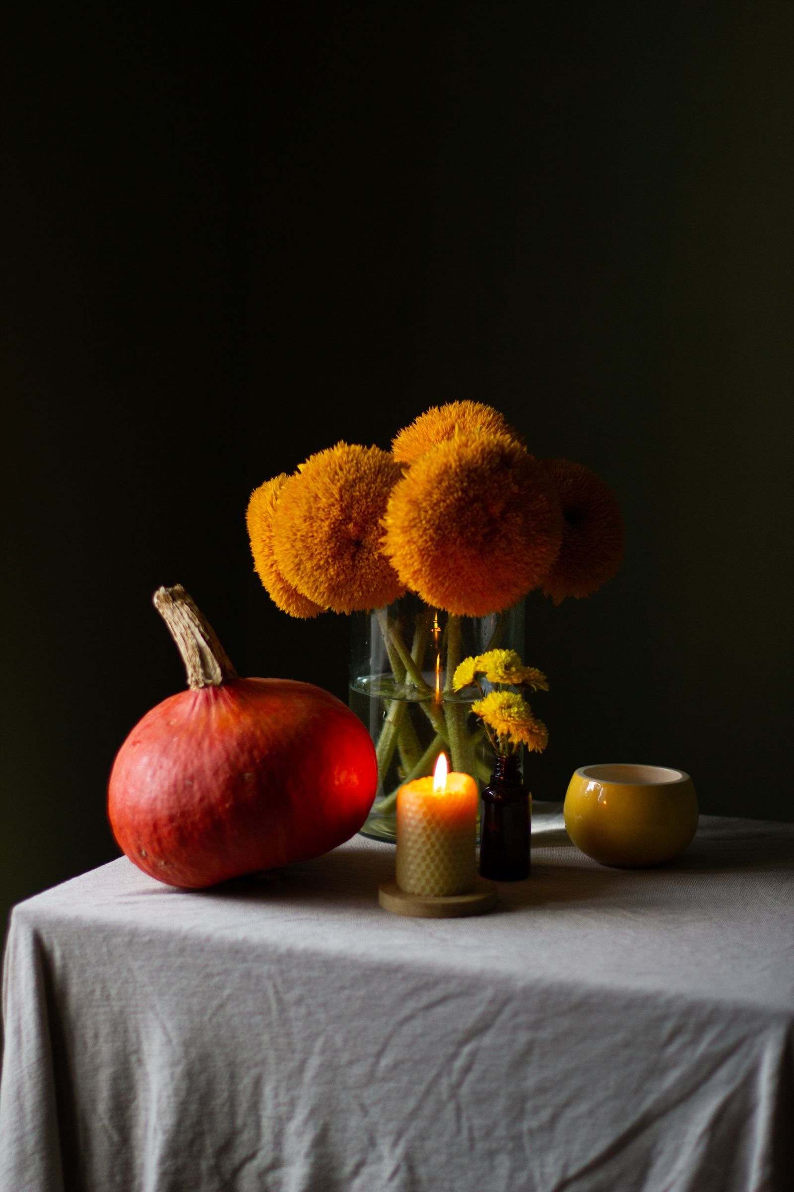 A small pumpkin beside flowers in a vase and a burning candle