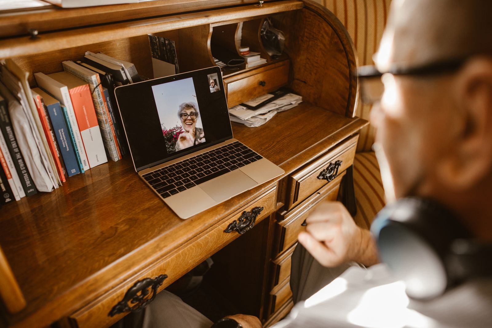 A laptop video call at a desk beside books