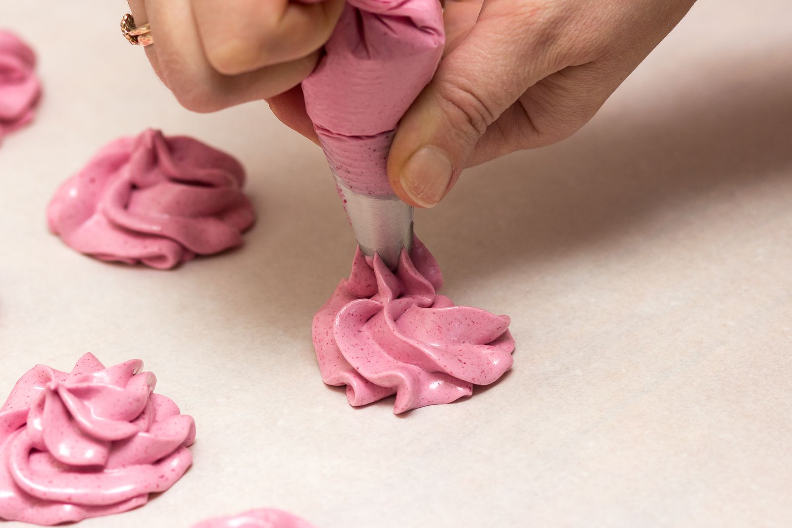 Hands piping pink meringue shapes through a decorating tip