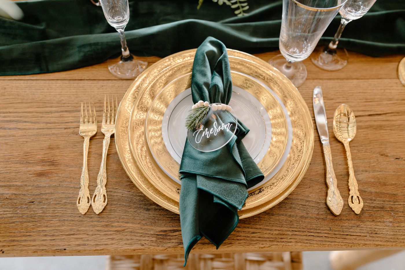 A green cloth napkin on gold and white plates at a festive place setting