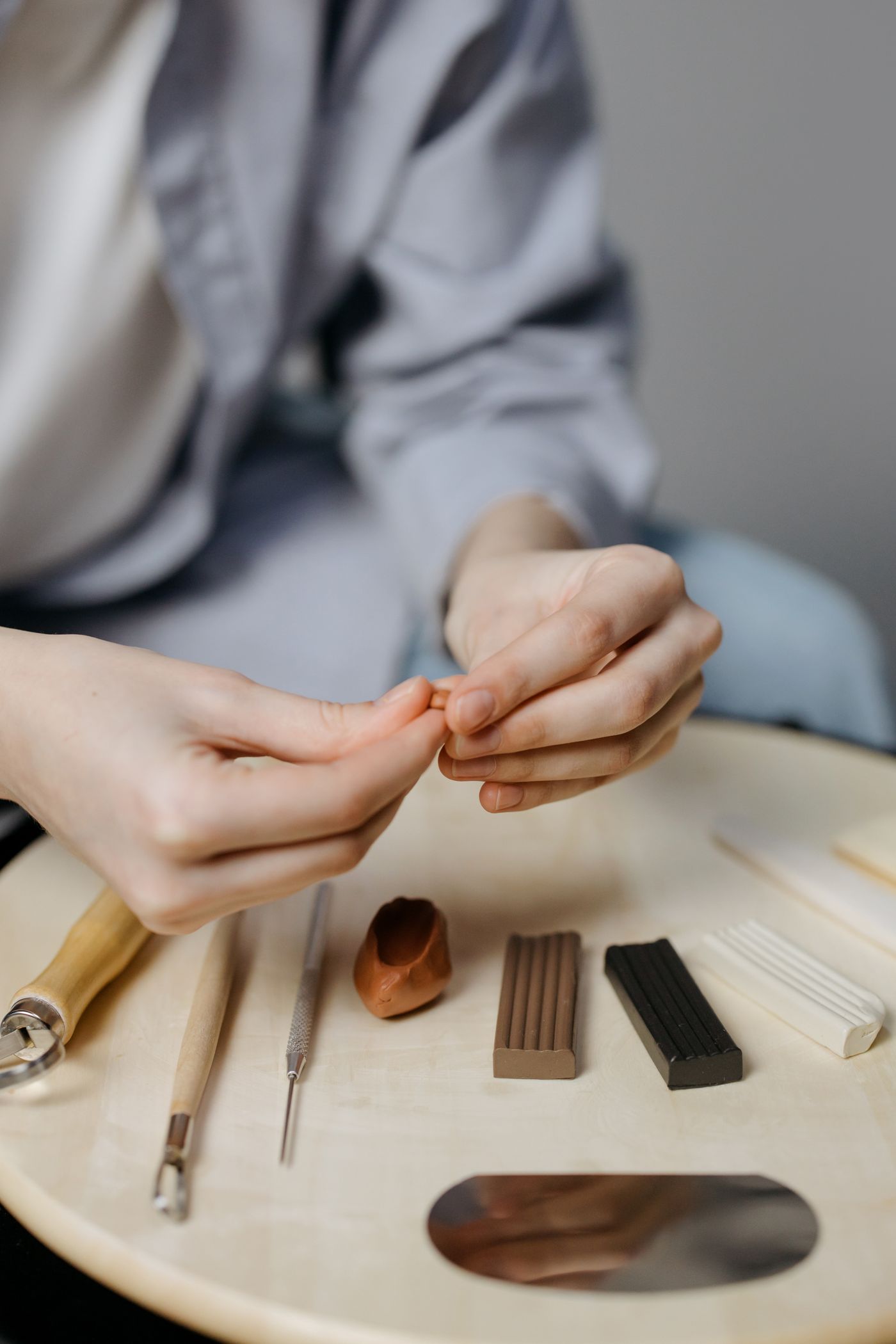 Hands shaping clay with tools at a work surface