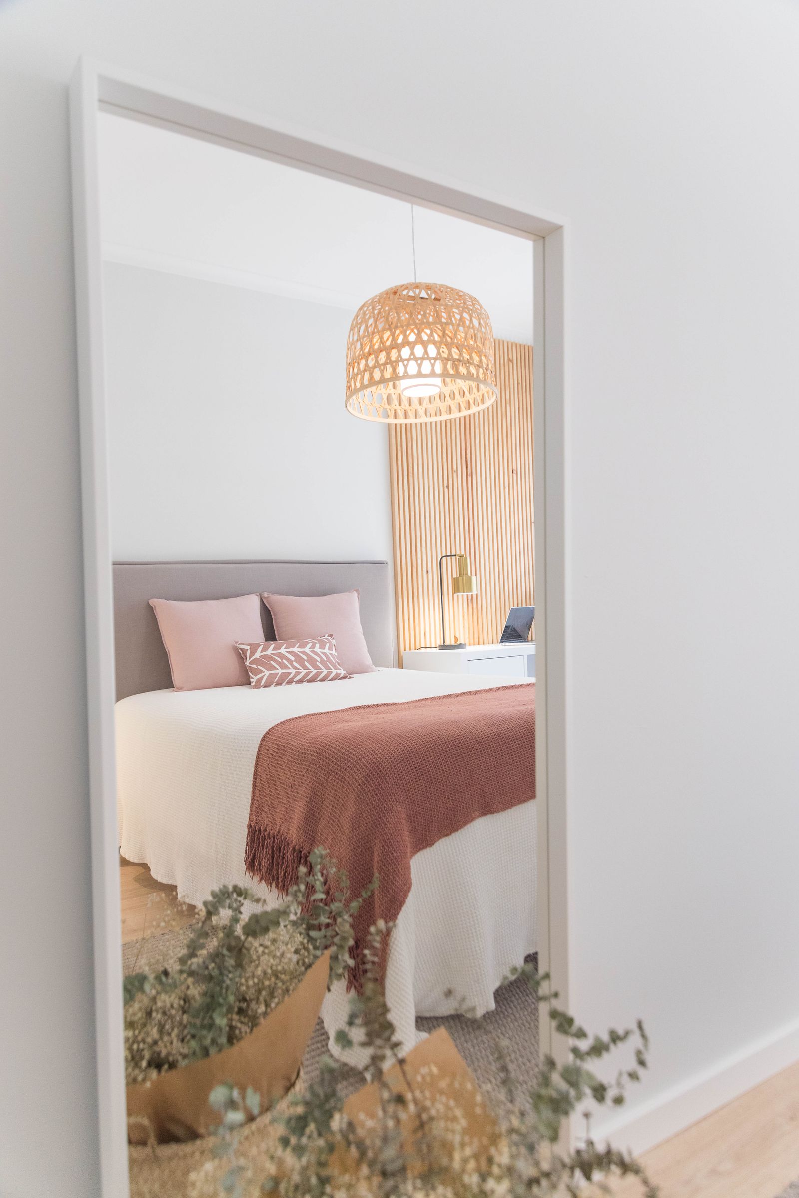 A tall mirror reflecting a bed and hanging lamp